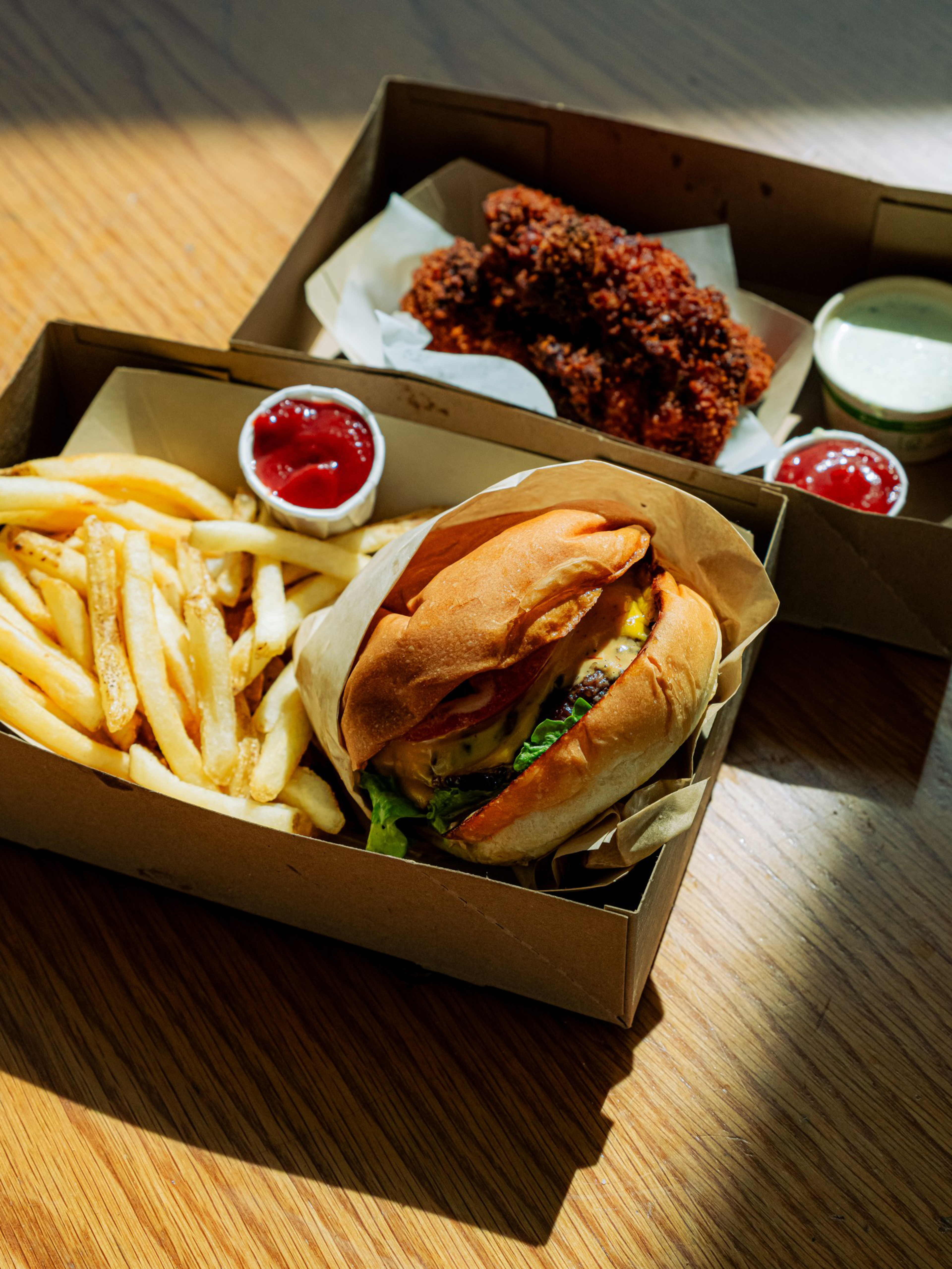 A meal with a cheeseburger, French fries, ketchup, crispy chicken tenders, and a small cup of white dipping sauce in cardboard takeout boxes.