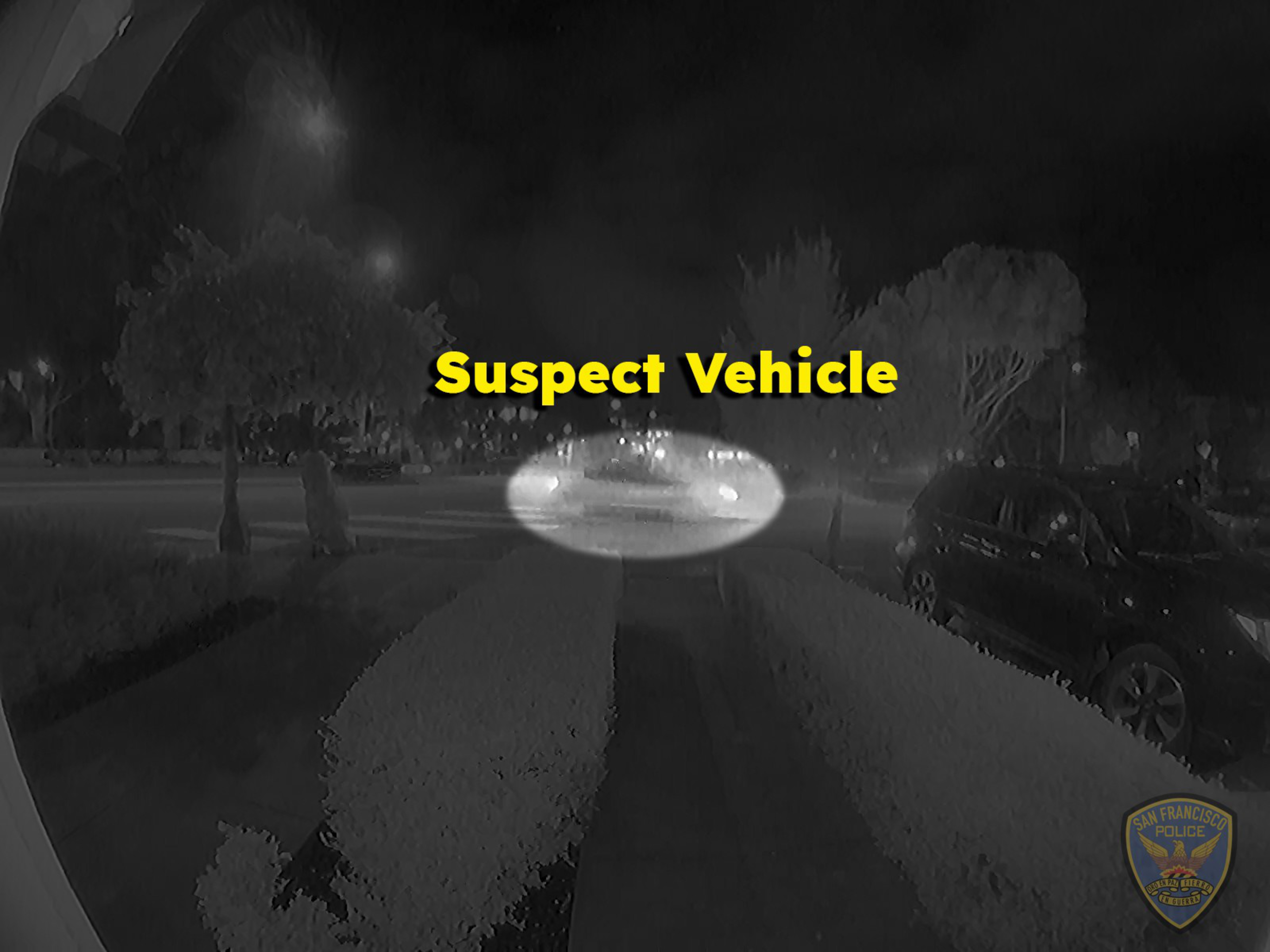 A car with its headlights on is driving on a street at night, highlighted by a white oval with the label "Suspect Vehicle" in bright yellow text.
