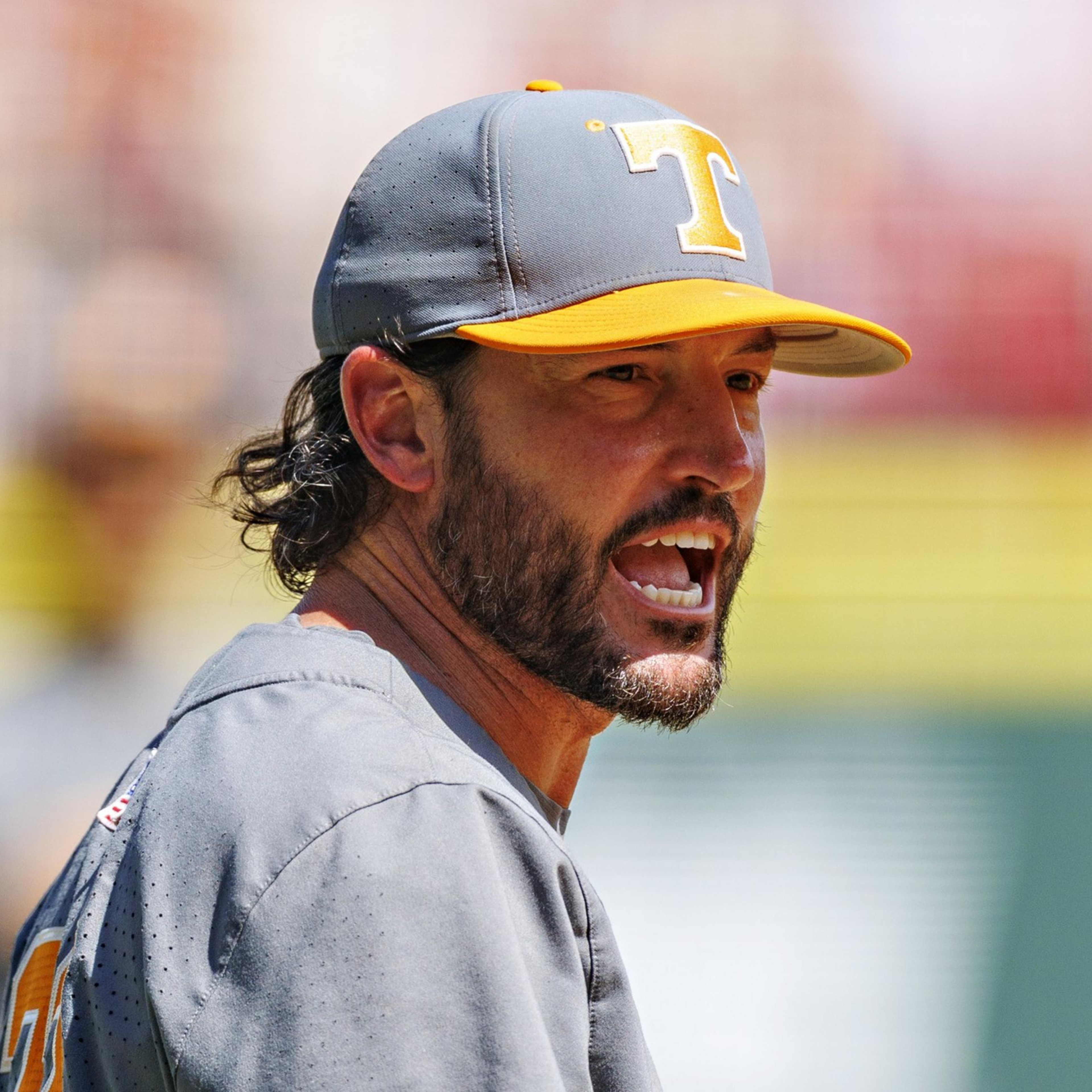 A man wearing a gray and orange baseball cap with a "T" on it is speaking passionately, wearing a gray shirt with an orange number.