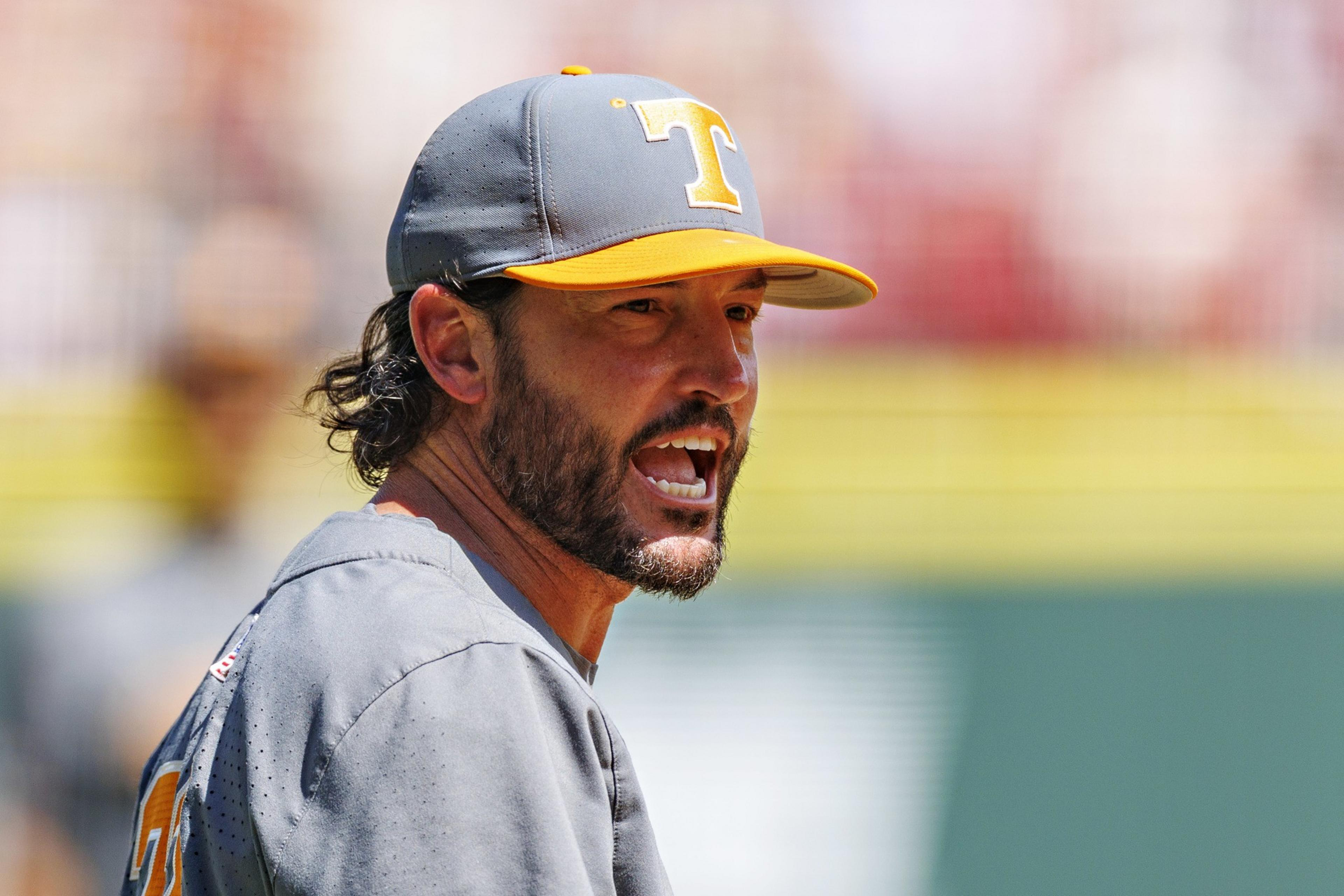 A man wearing a gray and orange baseball cap with a “T” on it is speaking passionately, wearing a gray shirt with an orange number.