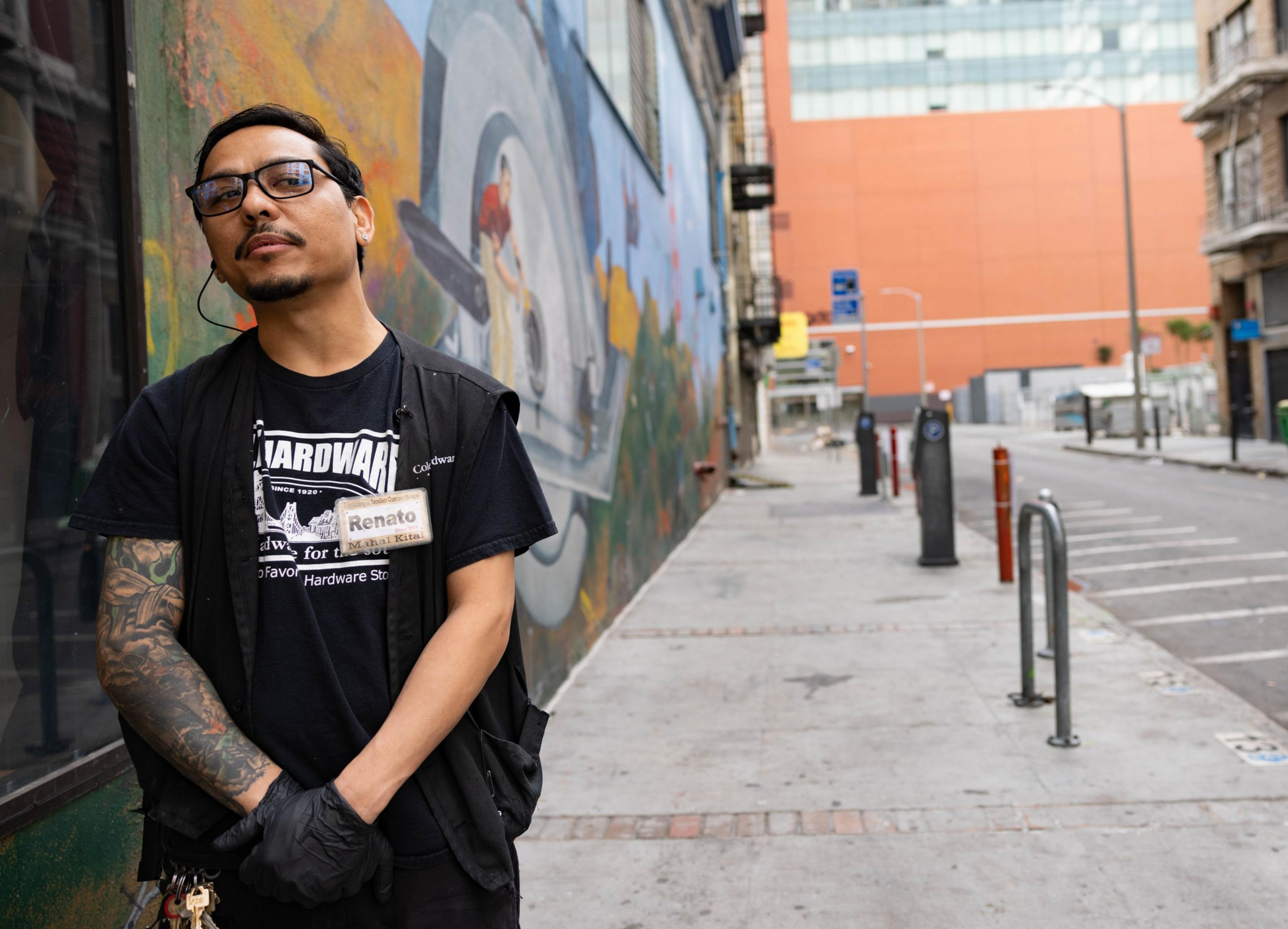 A man in a black T-shirt stands in front of a mural on the street. 