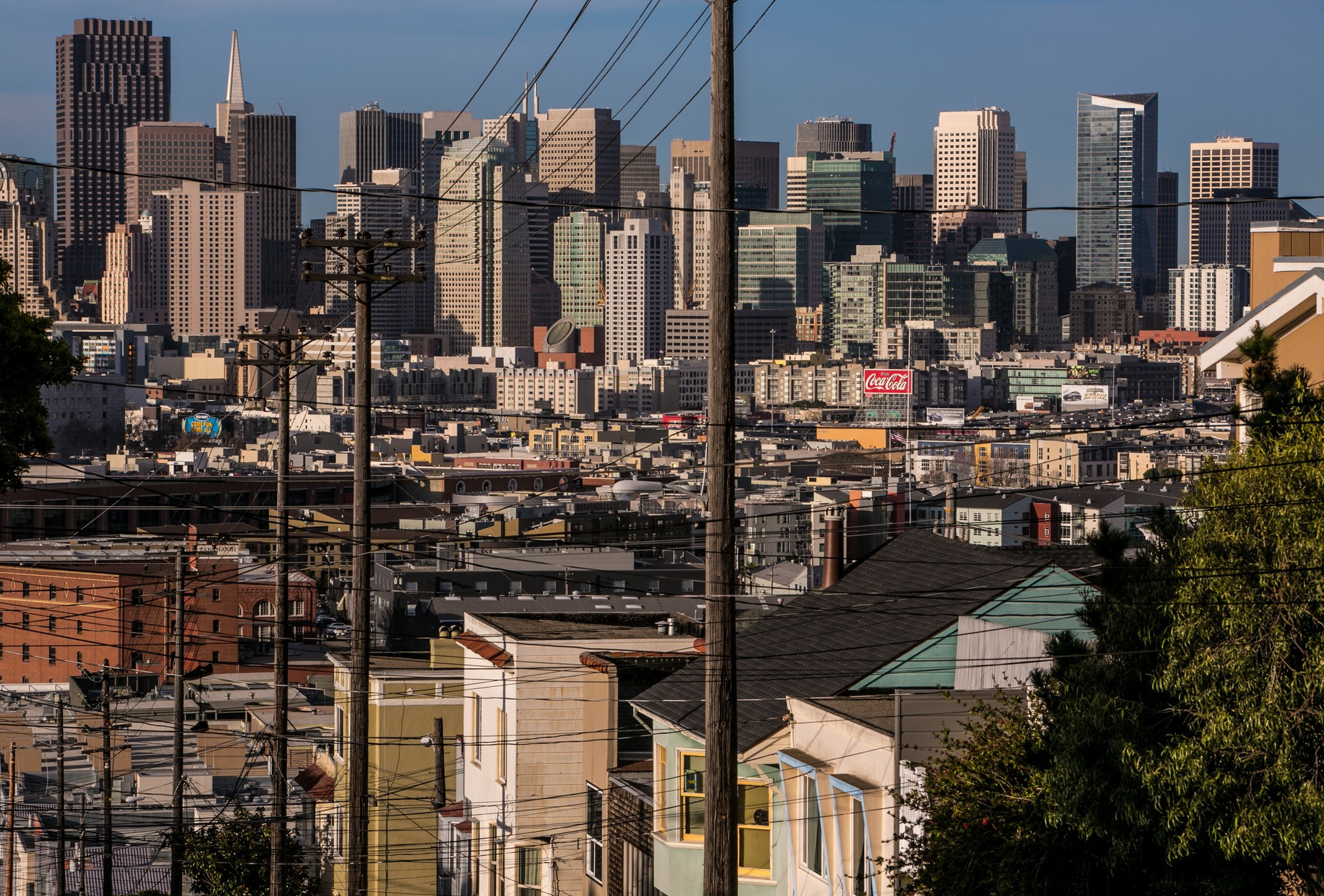 A dense cityscape with numerous skyscrapers in the background, residential houses in the foreground, and many power lines crossing the scene.