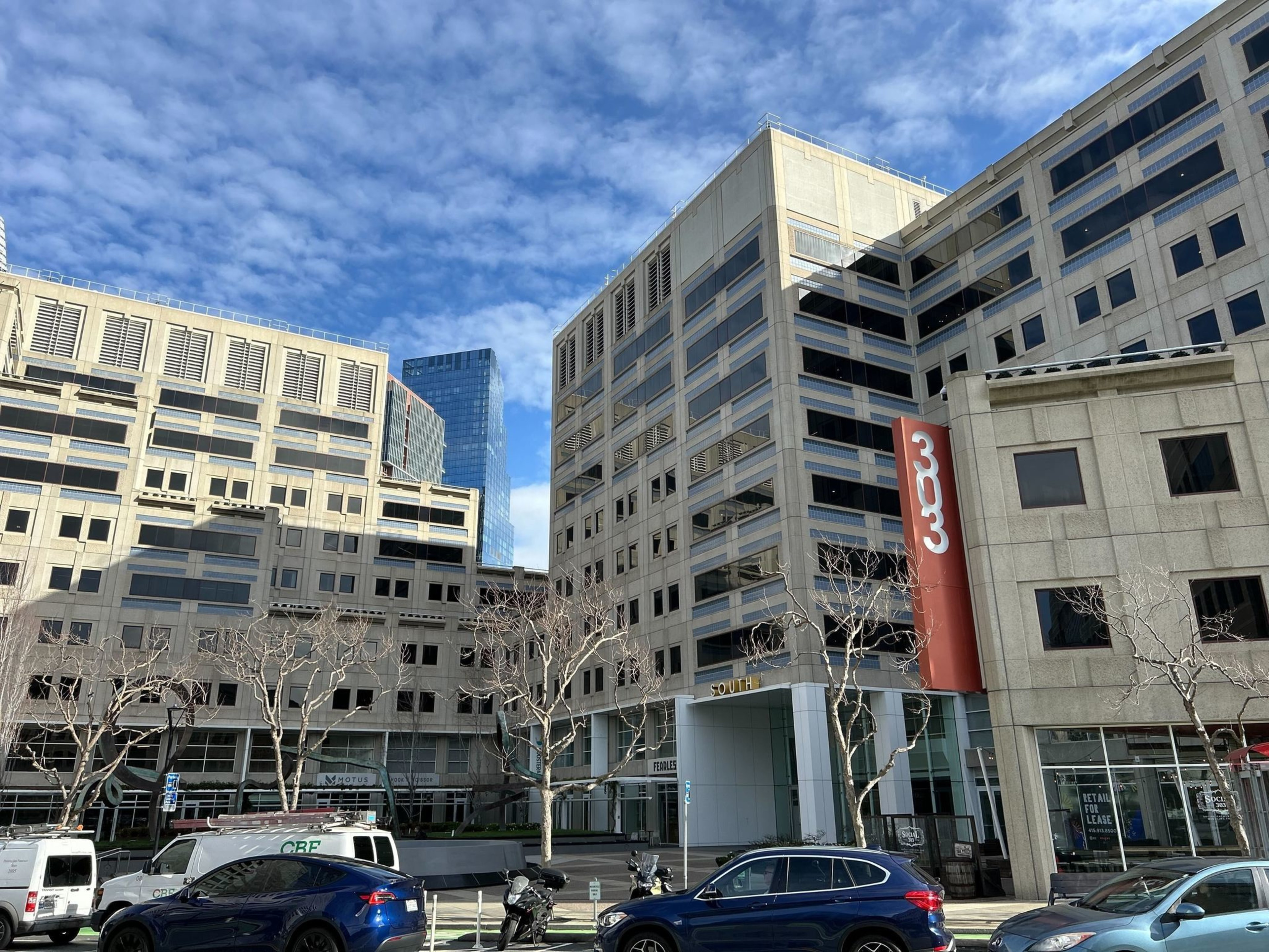Modern buildings with &quot;333&quot; sign, bare trees, and cars on a sunny day with blue sky.