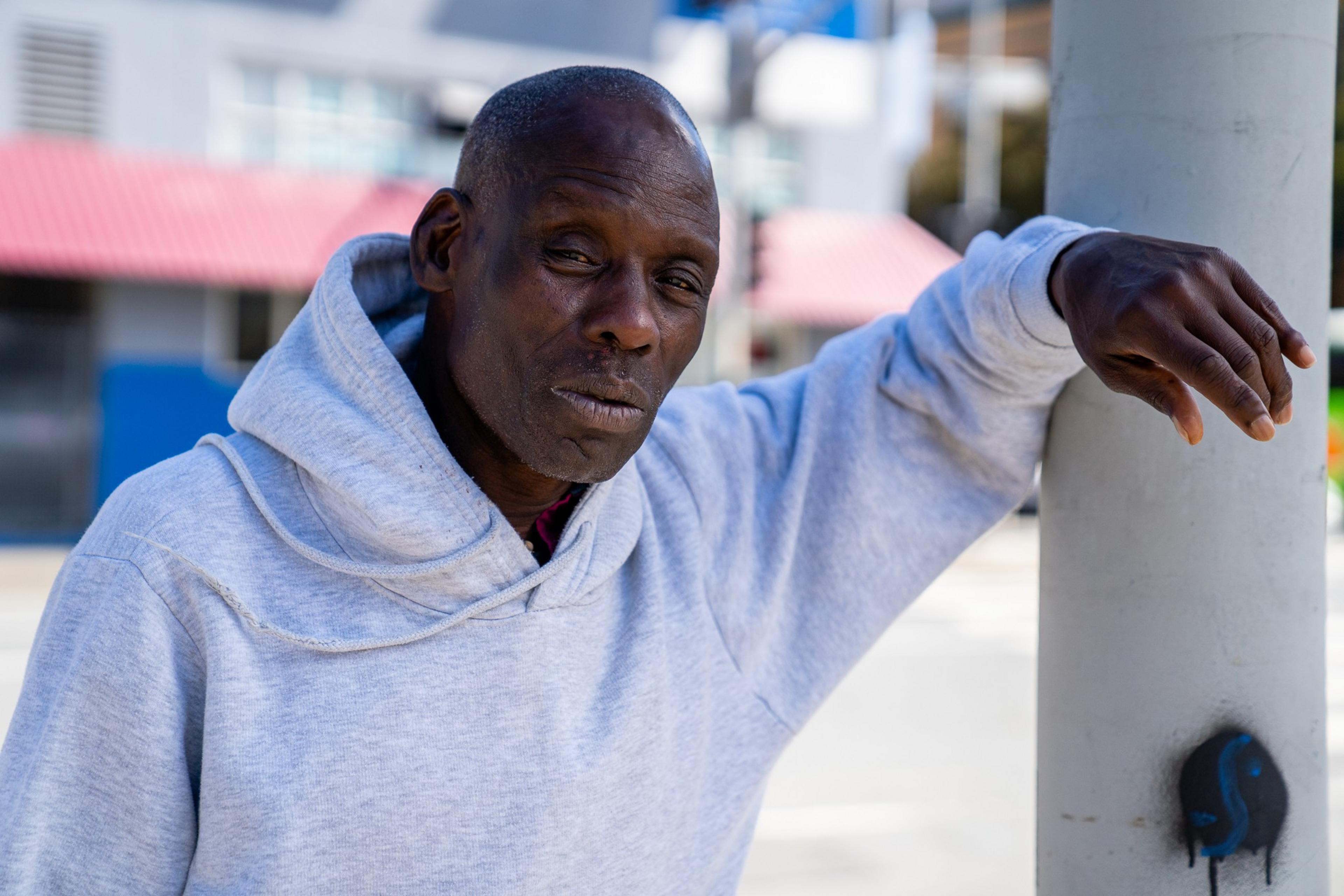 A person stands leaning against a pole wearing a white sweater
