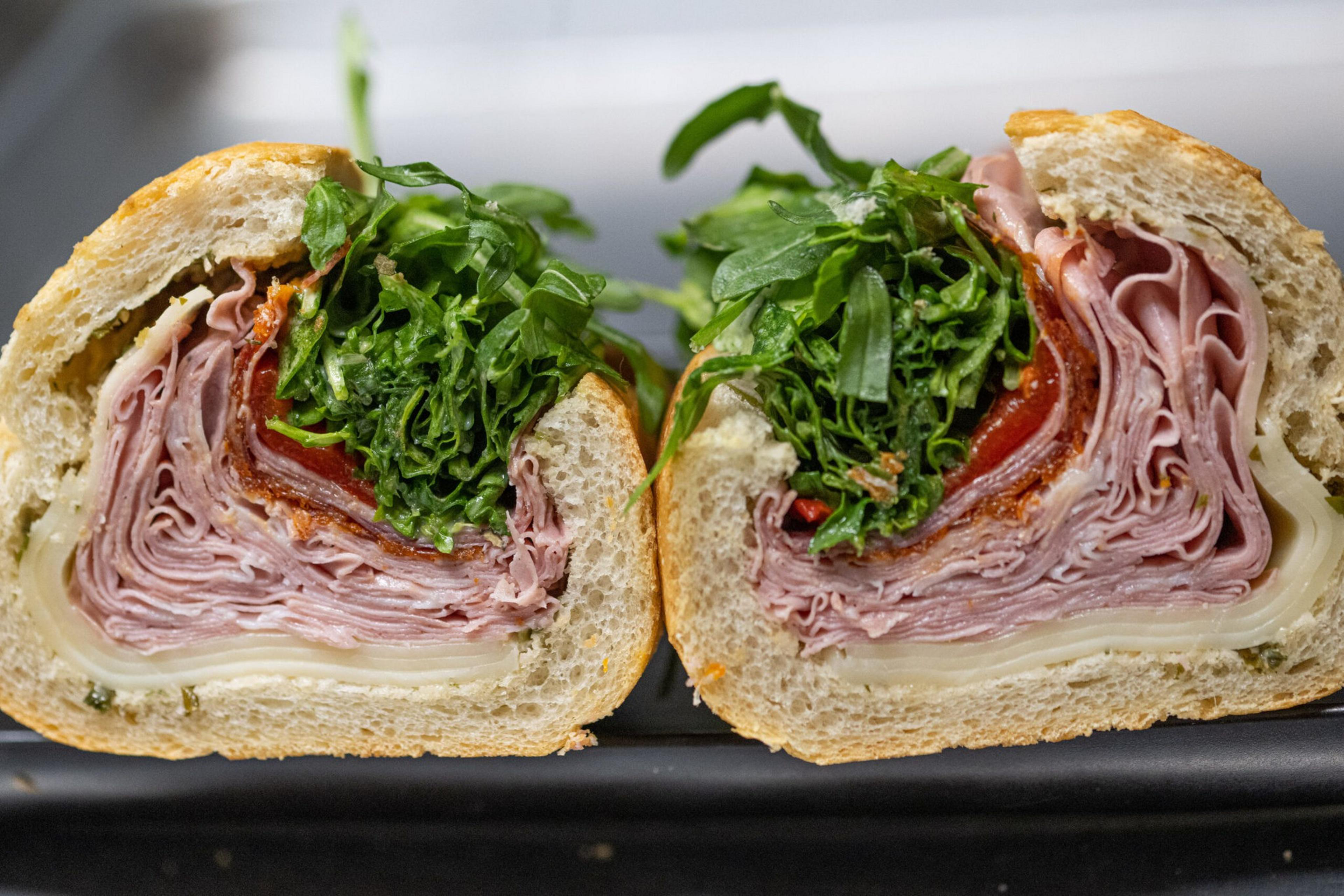 Two halves of a sandwich filled with layers of sliced ham, lettuce, tomato, and cheese inside a crusty sandwich roll.