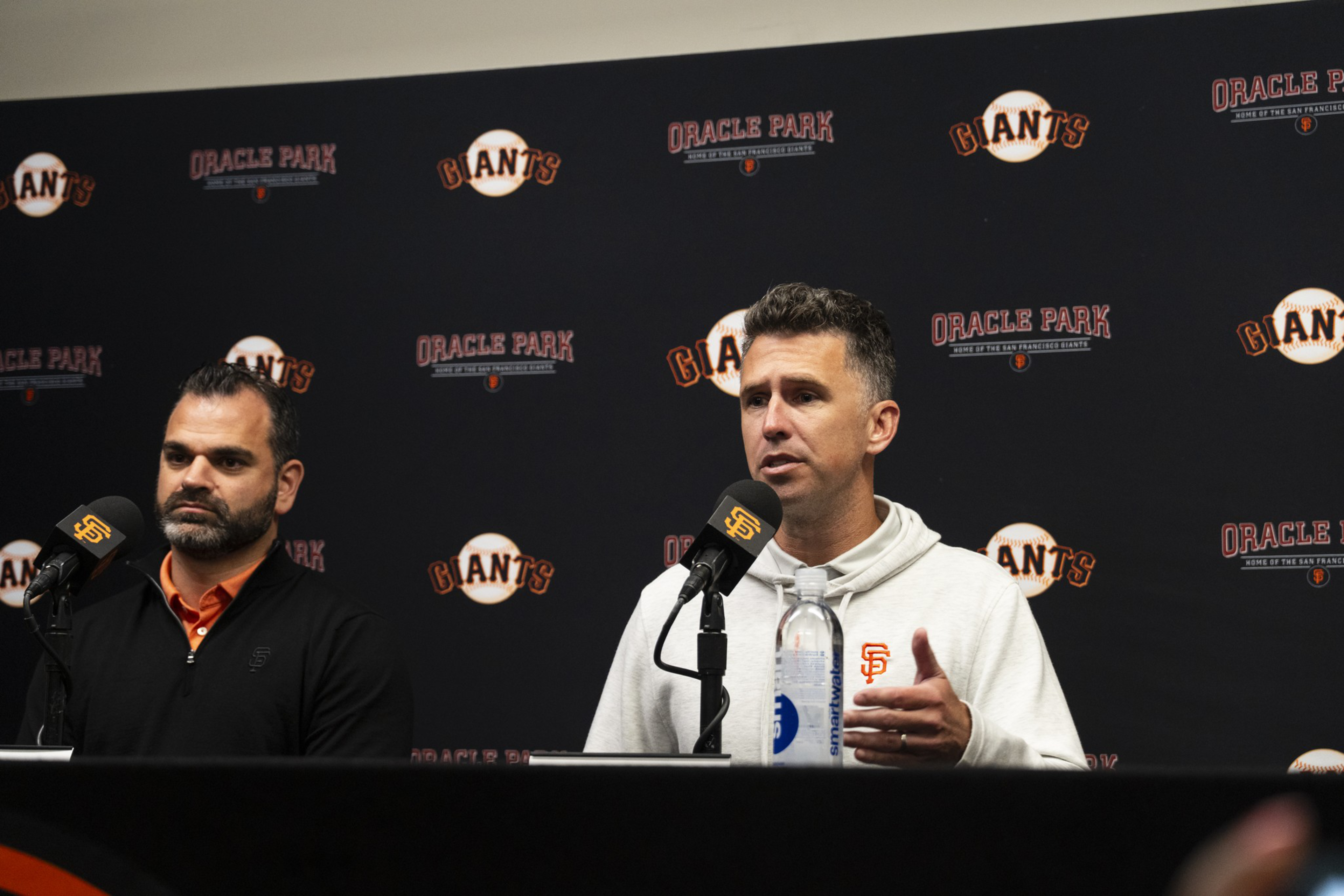 Two men sit at a press conference table with microphones, with an Oracle Park and Giants logo backdrop behind them.