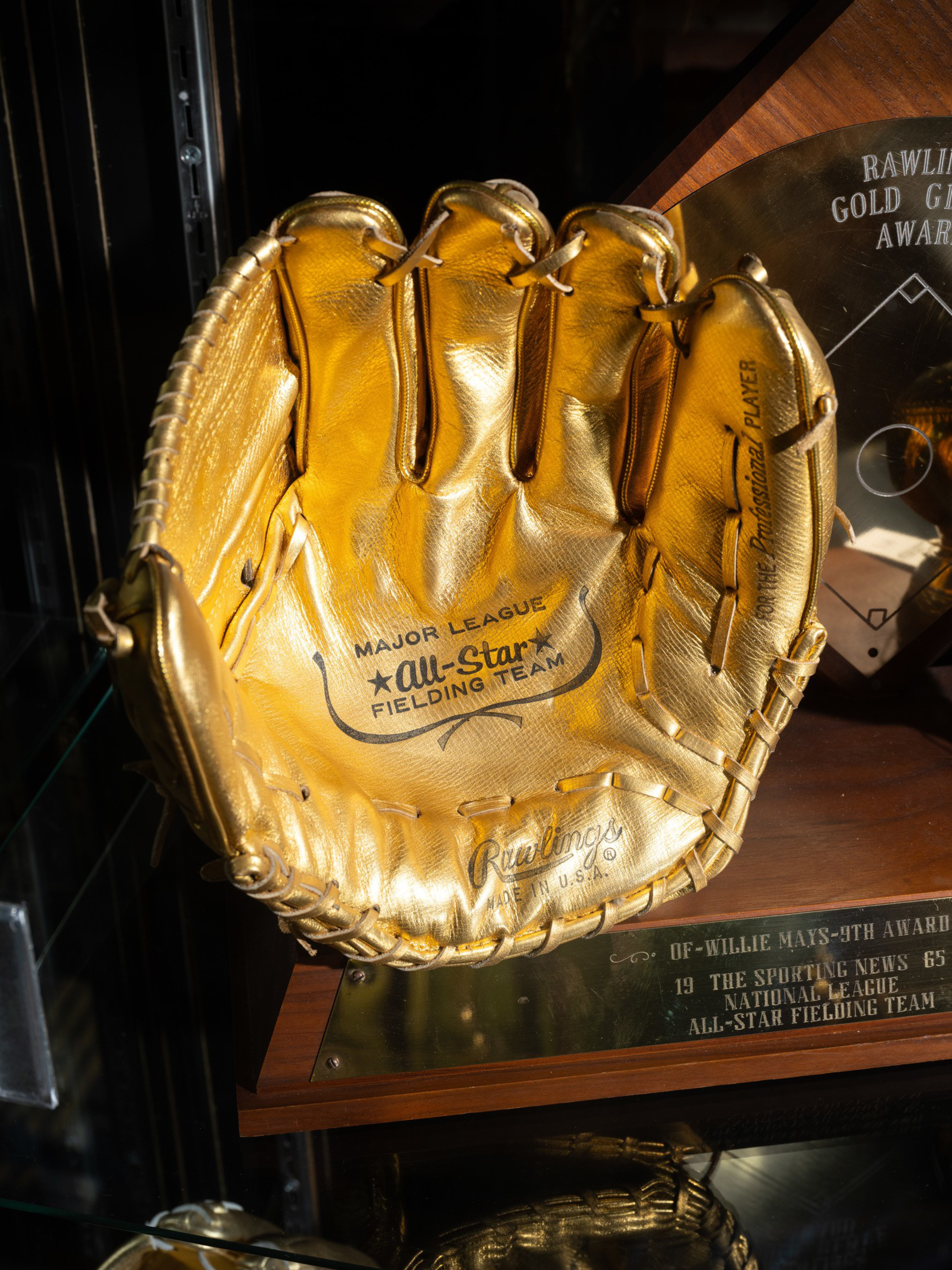A golden baseball glove labeled “Major League All-Star Fielding Team” sits mounted on a plaque honoring Willie Mays’s 1965 fielding award.