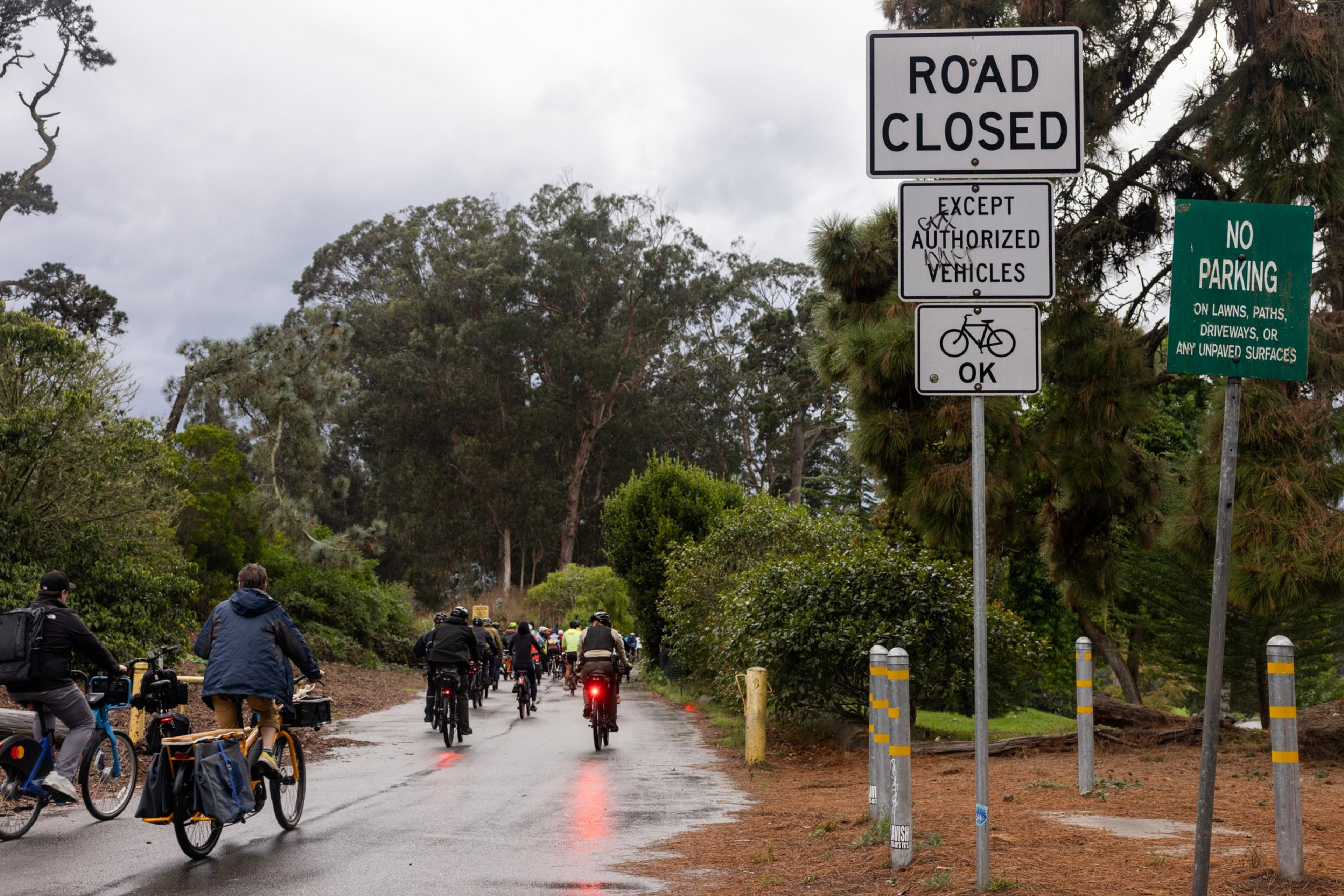 A group of people bike through the rain in Golden Gate Park.
