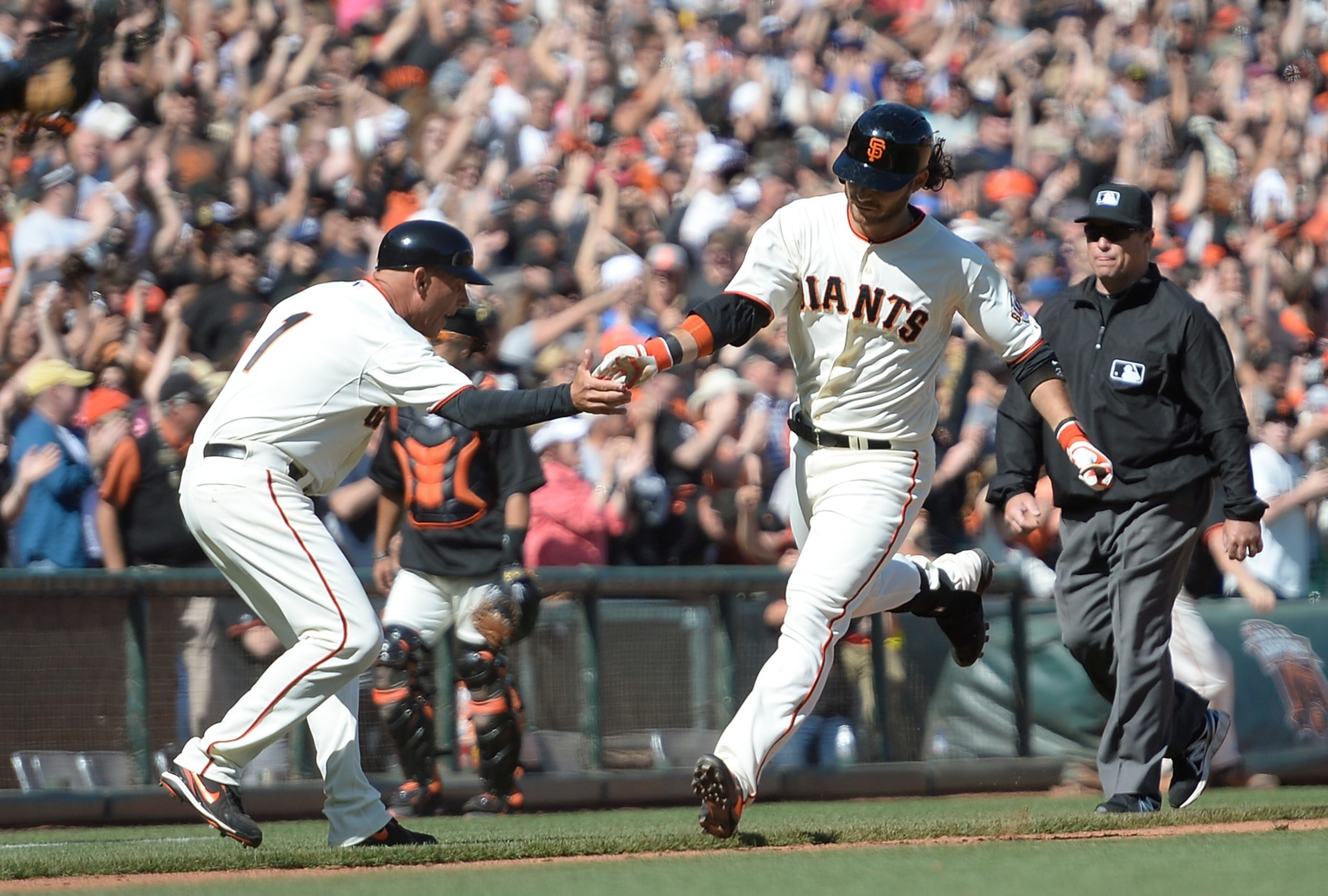 A baseball player from the Giants in a white uniform high-fives a coach while running. The crowd in the background cheers enthusiastically.