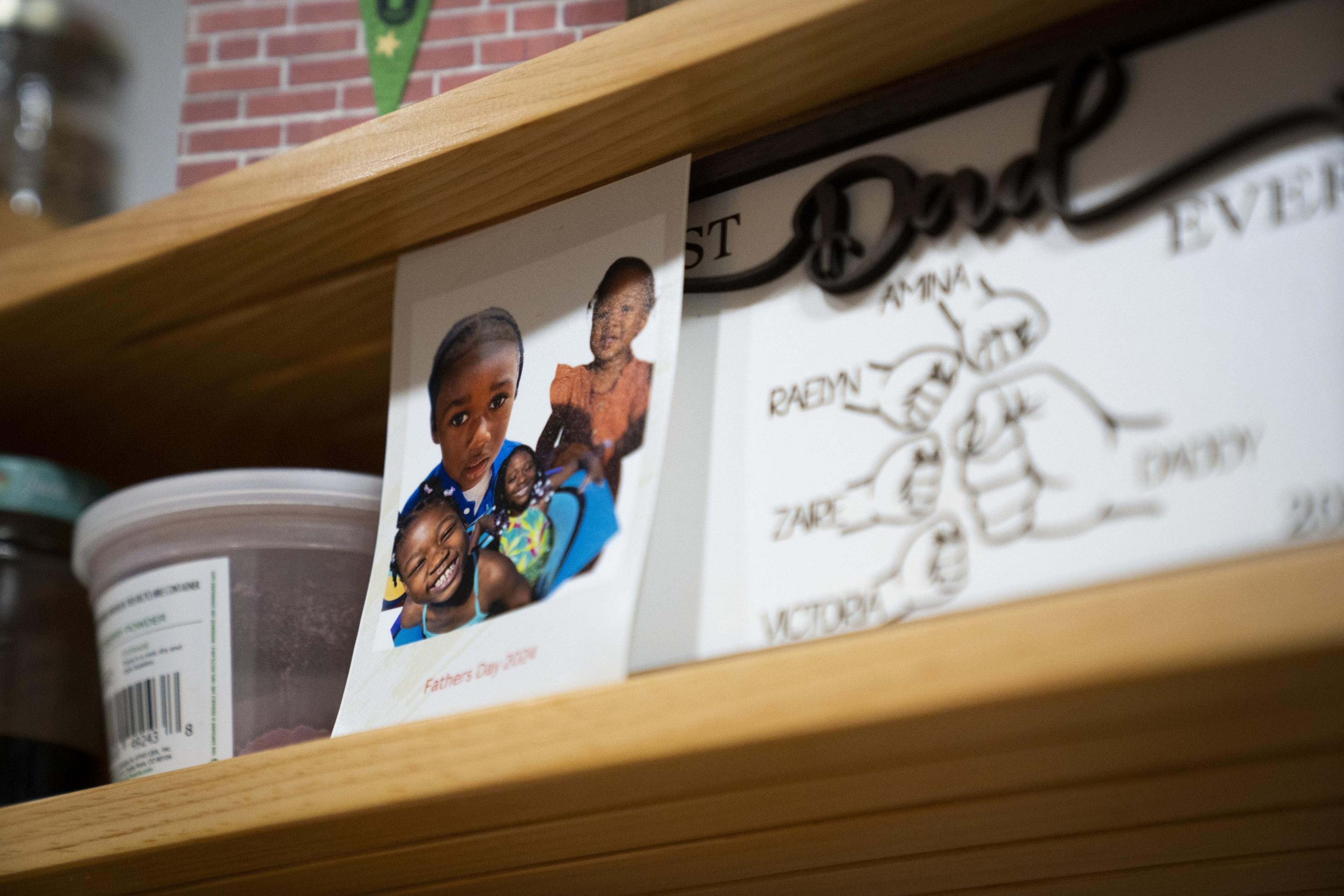 A photograph and a drawing on a wooden shelf. The photo shows smiling children with &quot;Fathers Day 2020&quot; printed below. The drawing features fists with names.