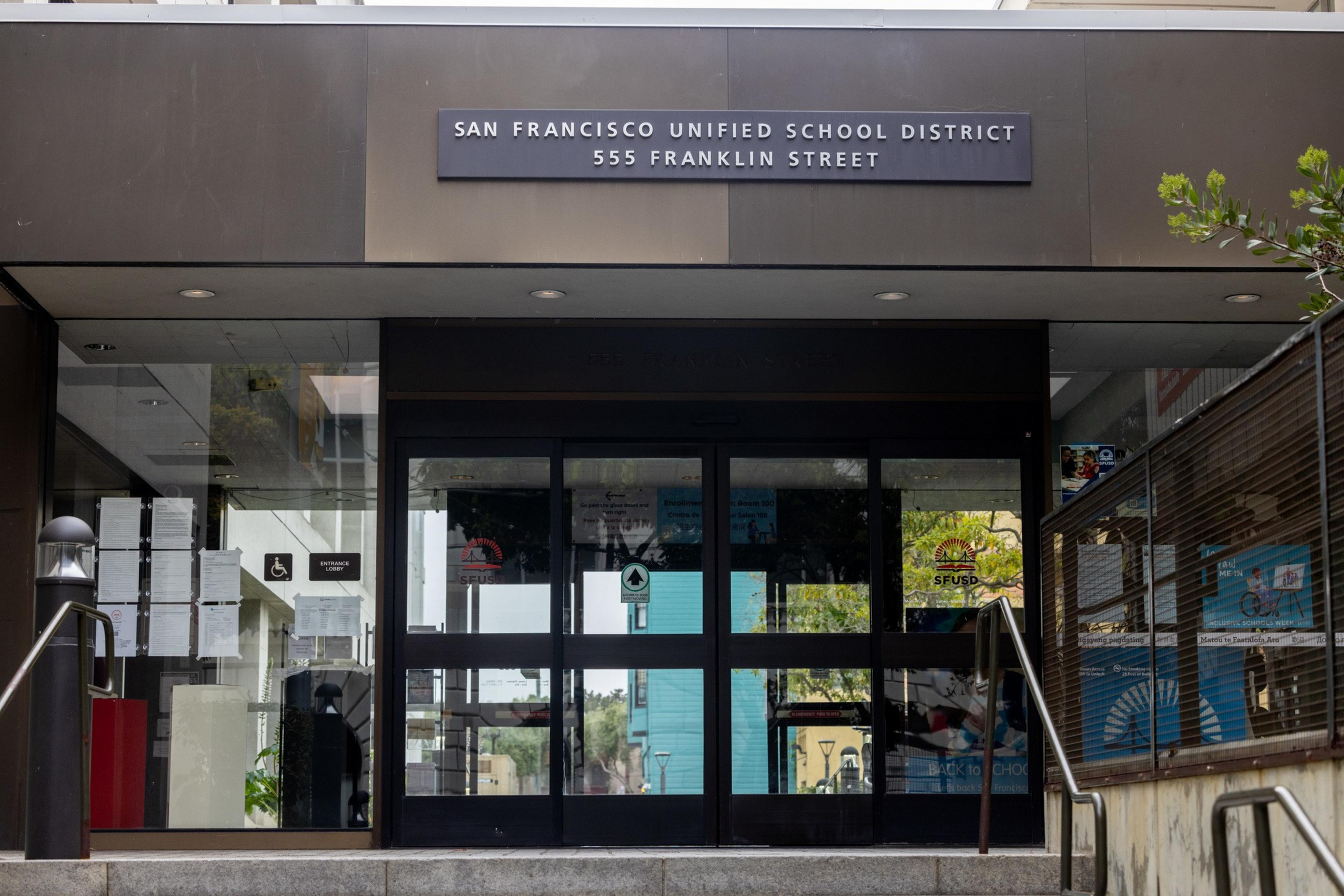 The image shows the entrance of the San Francisco Unified School District at 555 Franklin Street. It has a glass door with visible signs and notice boards.