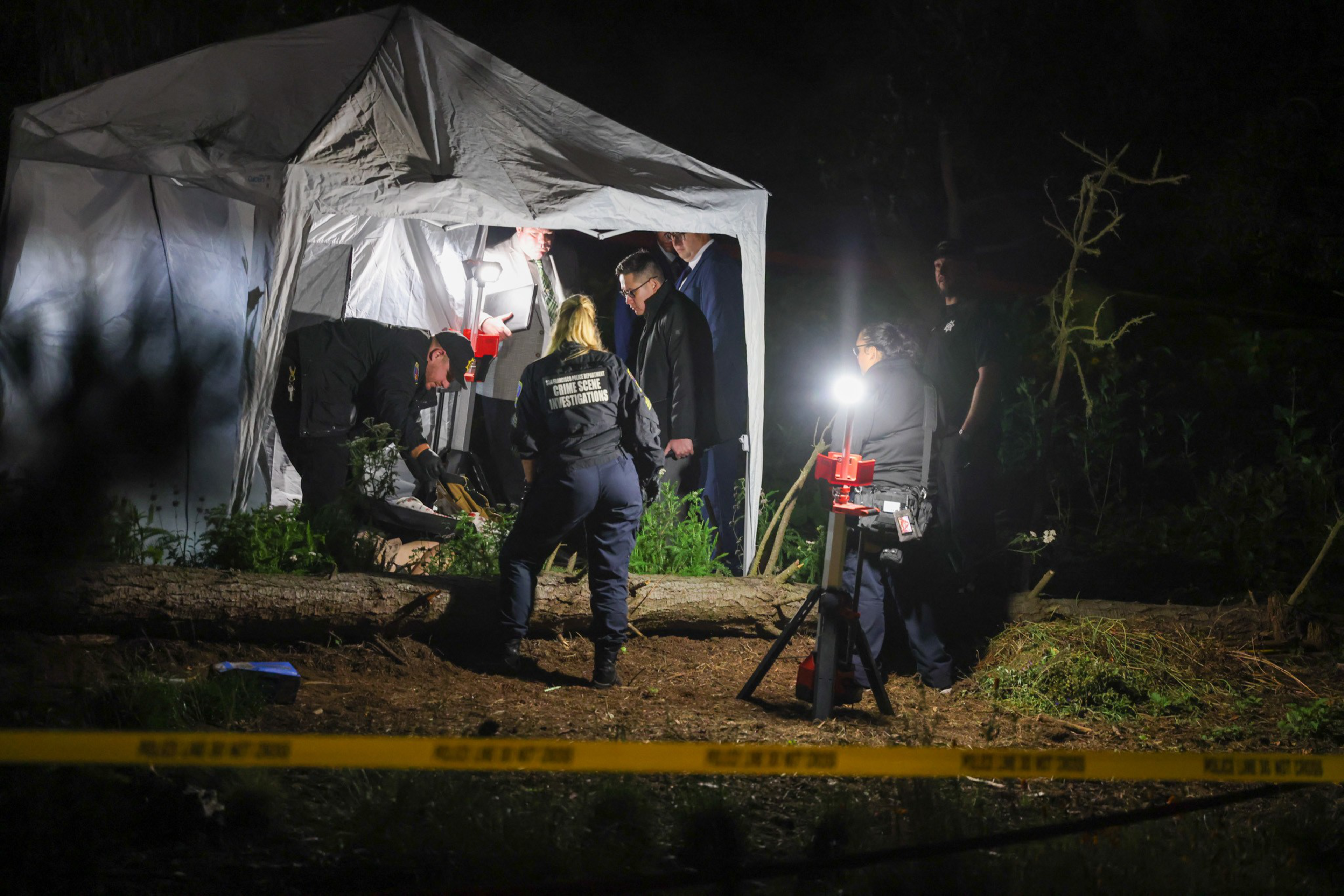 Law enforcement personnel stand beneath a white canopy lit by white lights late at night.