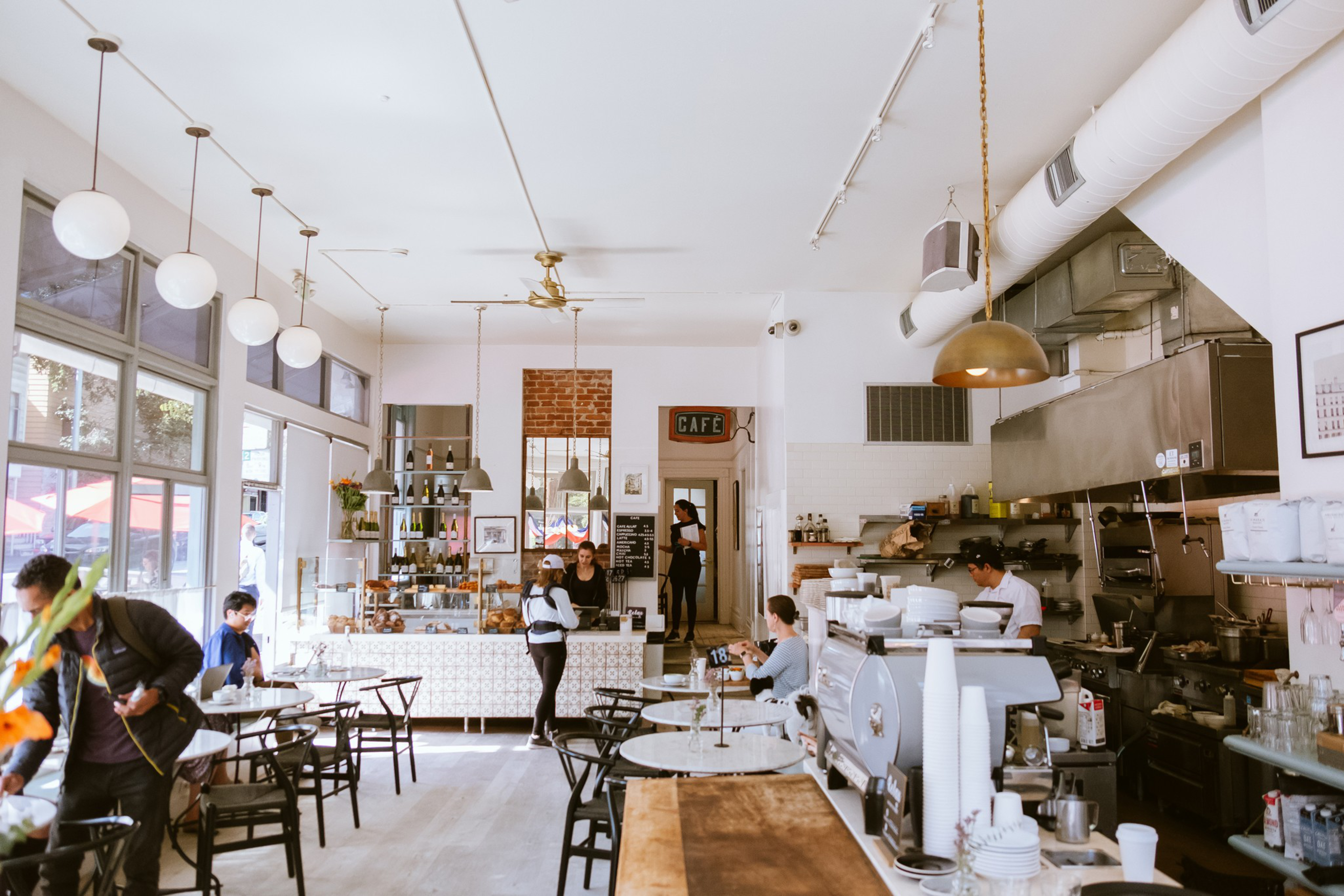 A cozy cafe interior with customers, pendant lights, an exposed brick wall, and a busy counter area.
