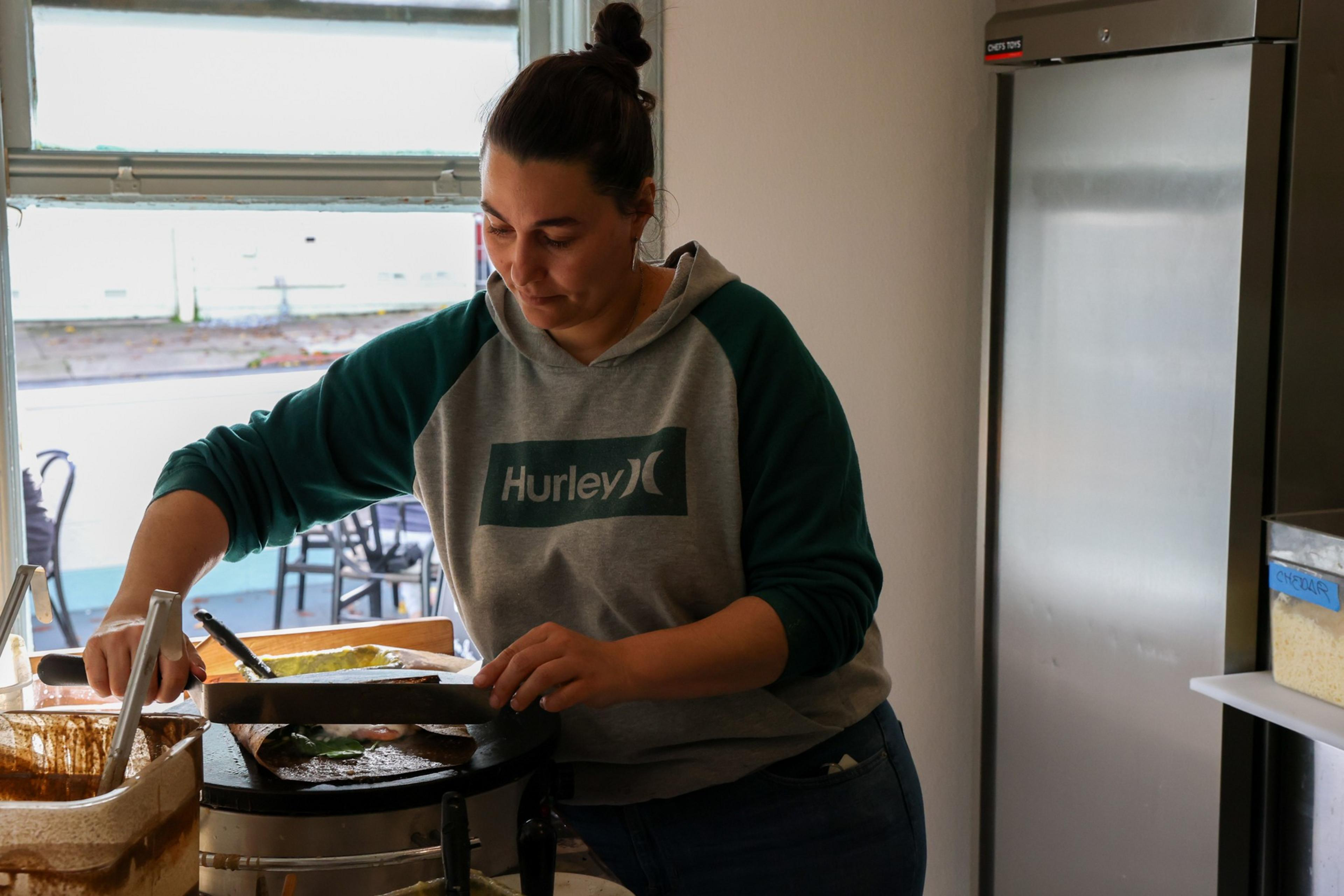 A woman folds a crepe in a sunlit kitchen.