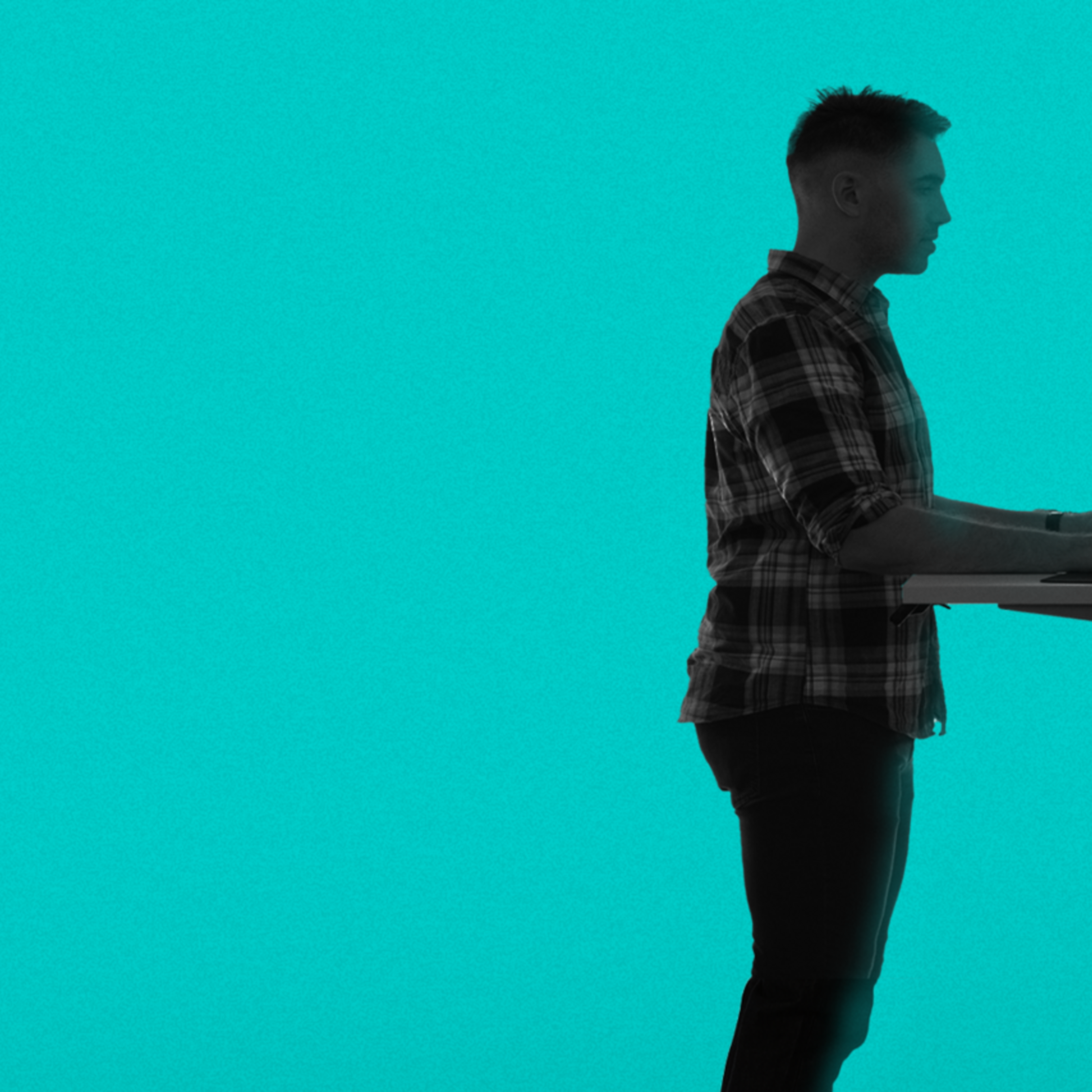 A person stands at a height-adjustable desk using a computer. Their shadow on the floor has a wavy pattern. The background is a solid teal color.