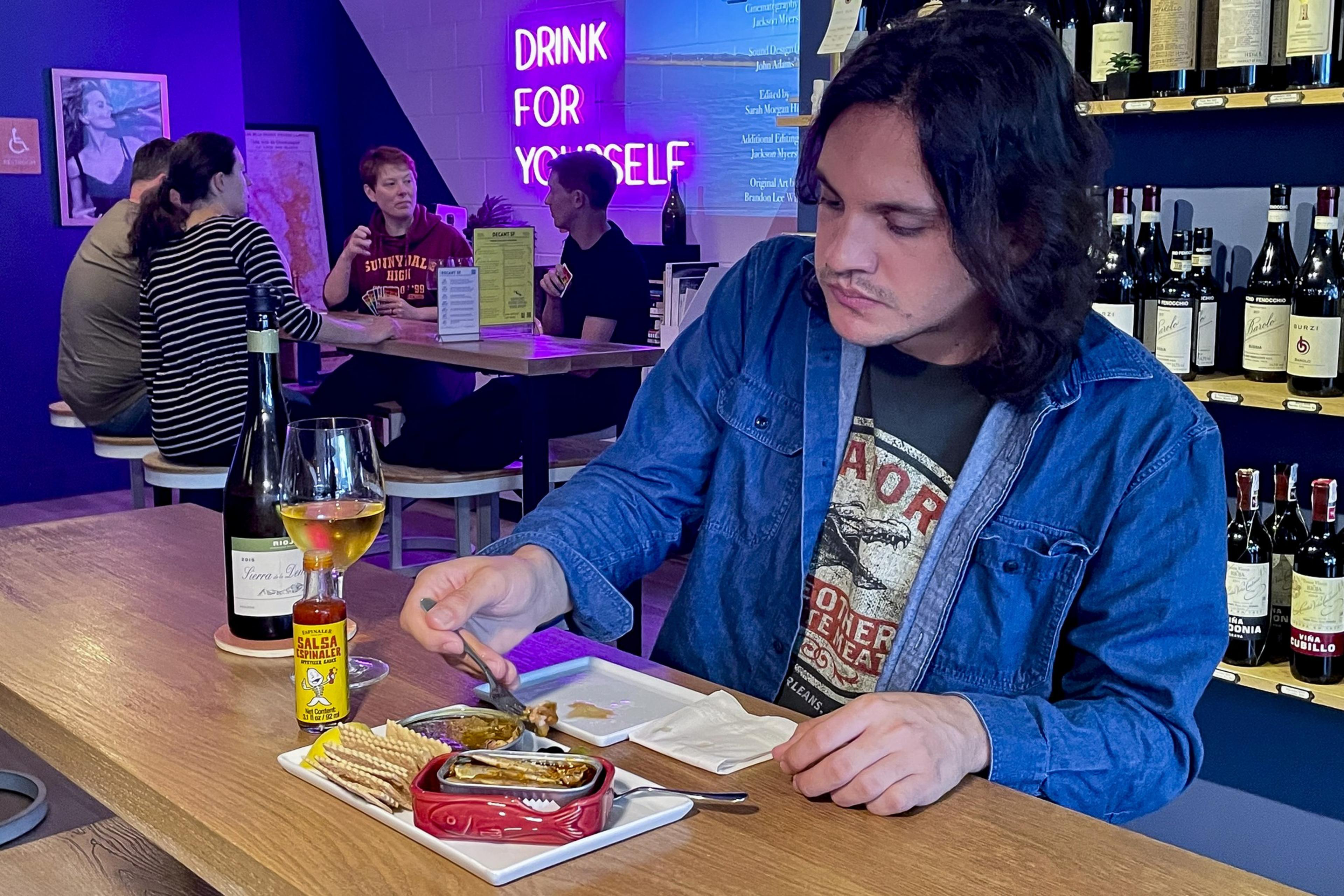A wine bar customer eats tinned fish at a counter.