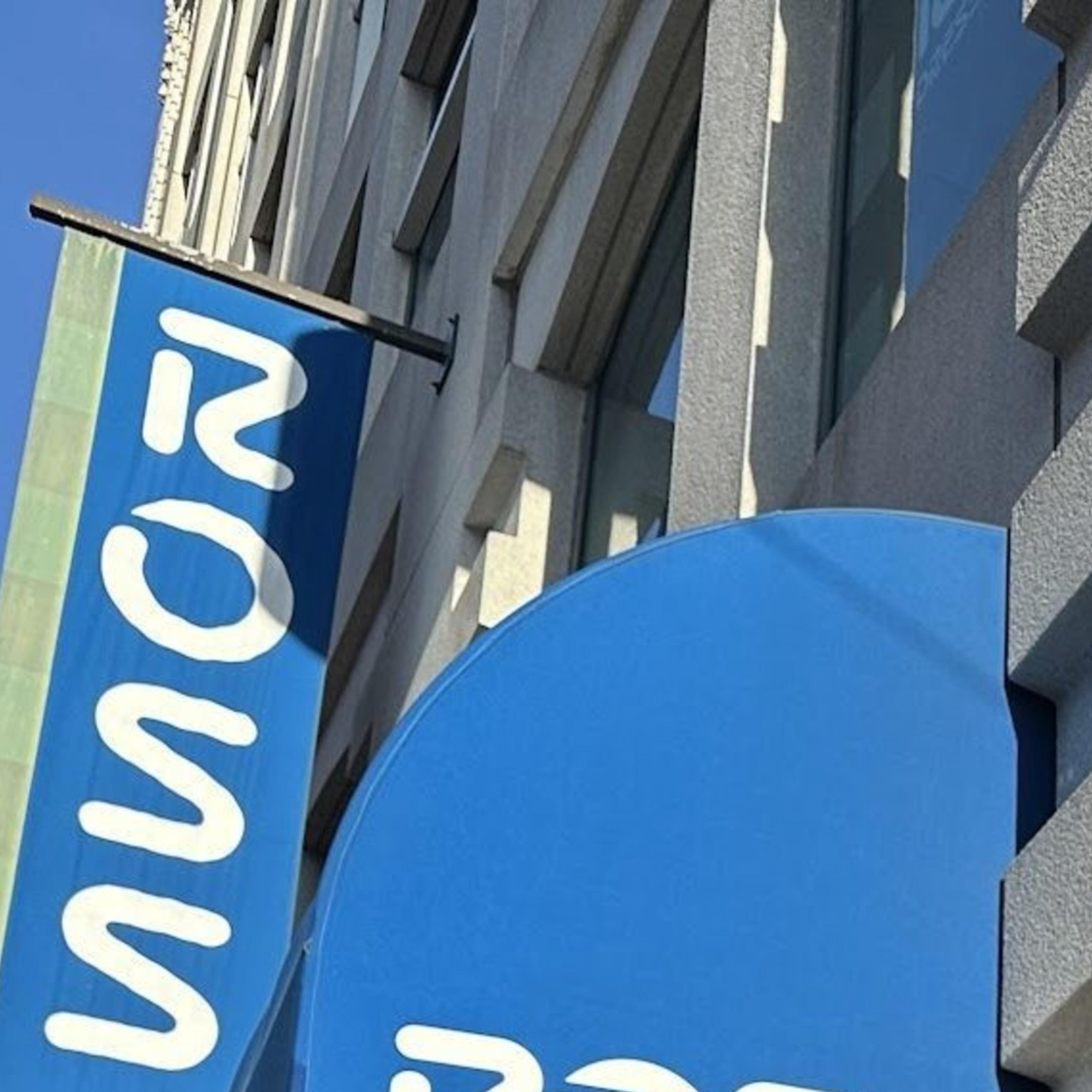 Two people are smiling outside a store with blue awnings displaying the word "ROSS." Another two people are to the left, one pointing towards the store.