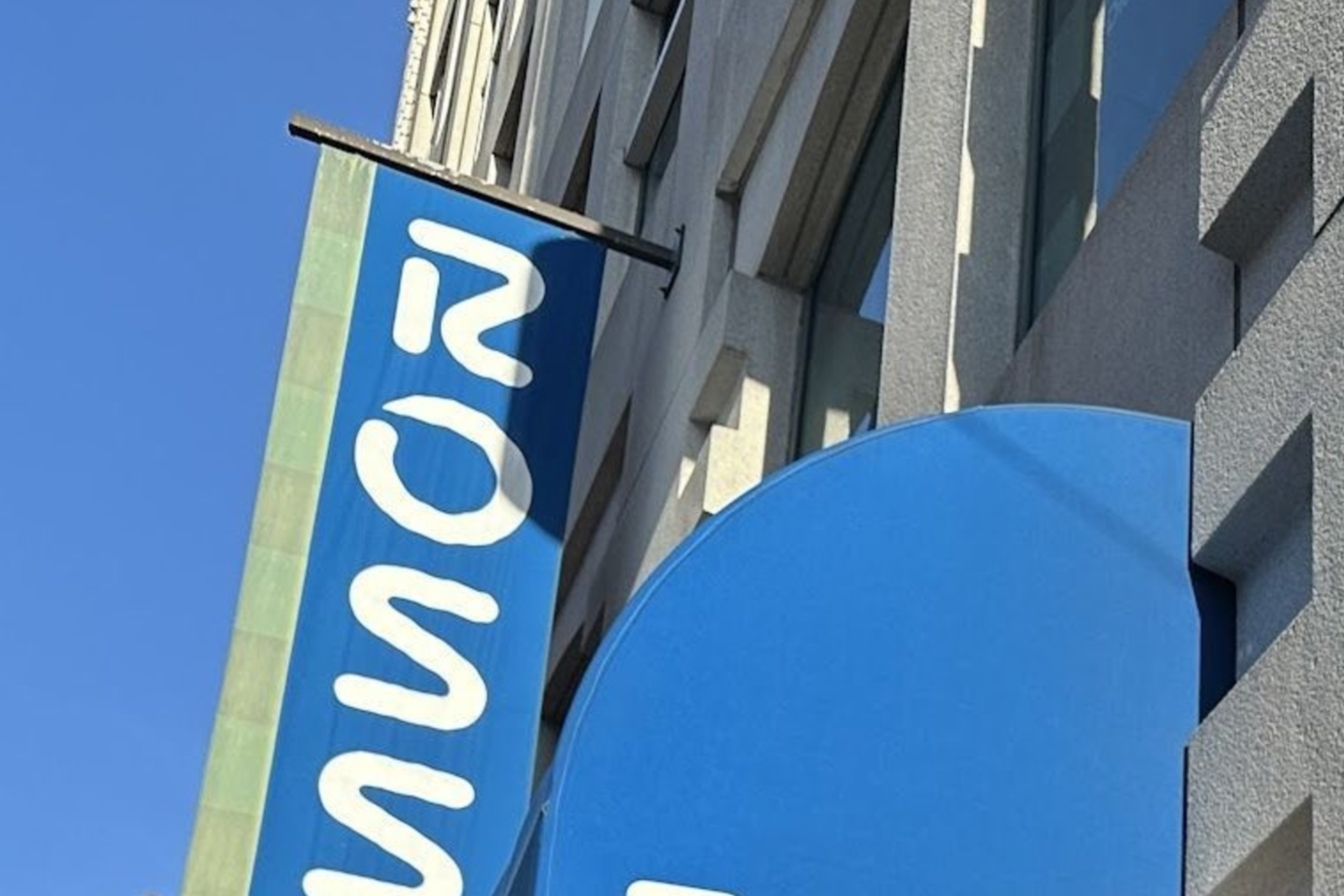Two people are smiling outside a store with blue awnings displaying the word "ROSS." Another two people are to the left, one pointing towards the store.