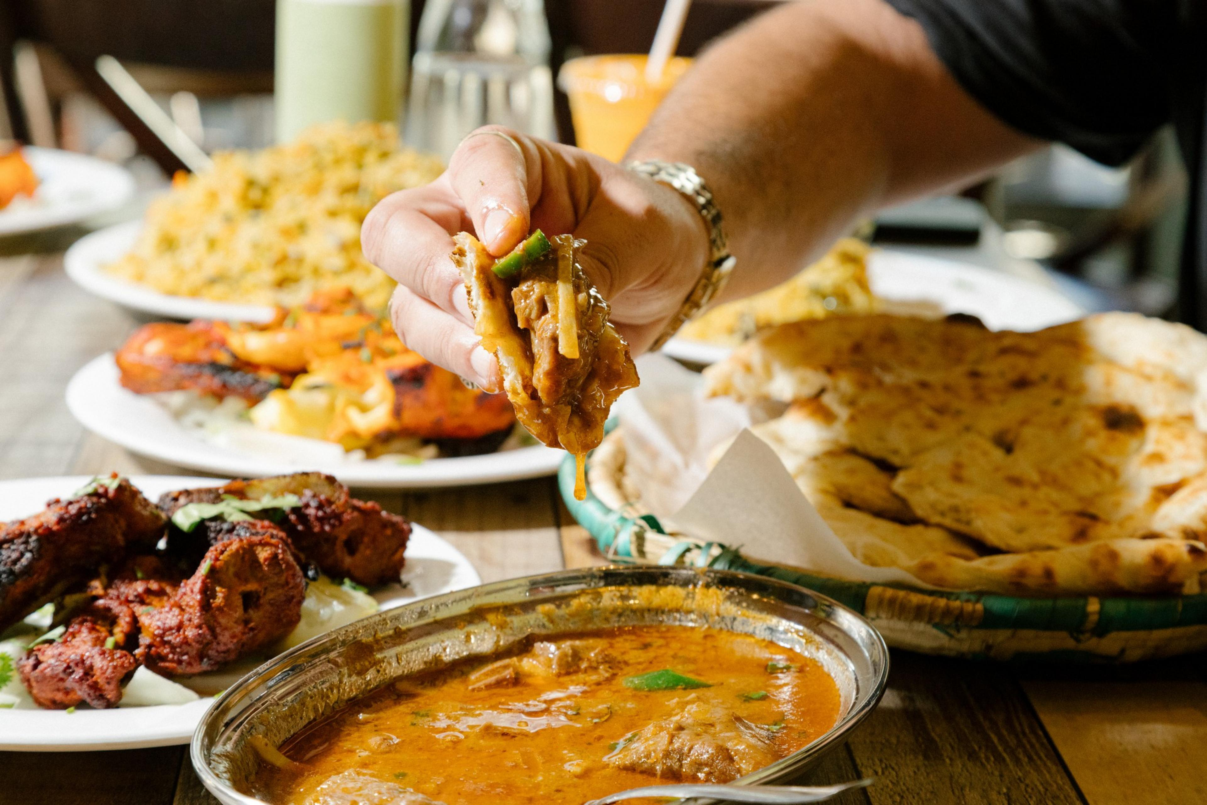 A hand is seen dipping freshly made naan into the nihari dish at Pakwan.