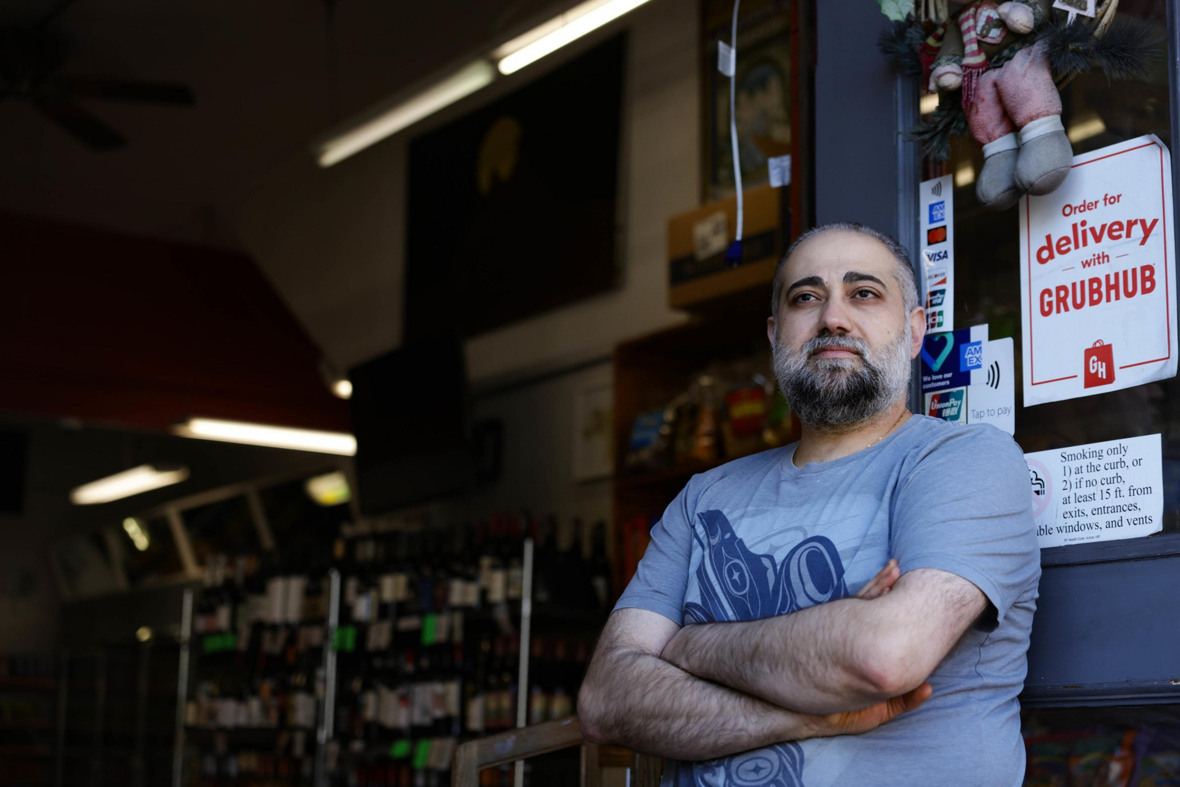 A man stands in the doorway of his business, arms crossed.