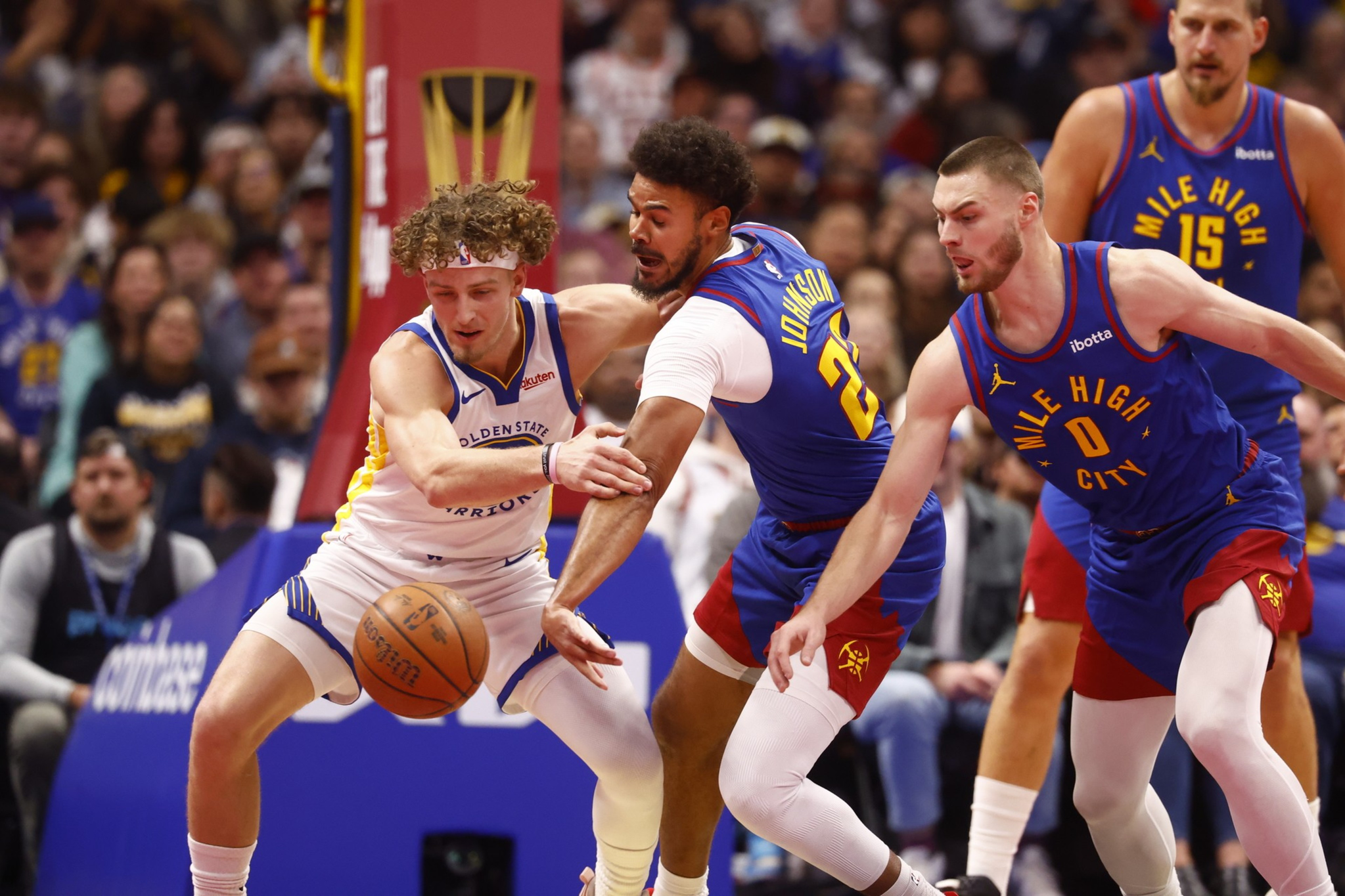 A Golden State Warriors player battles two Denver Nuggets defenders for control of a loose basketball during a game.