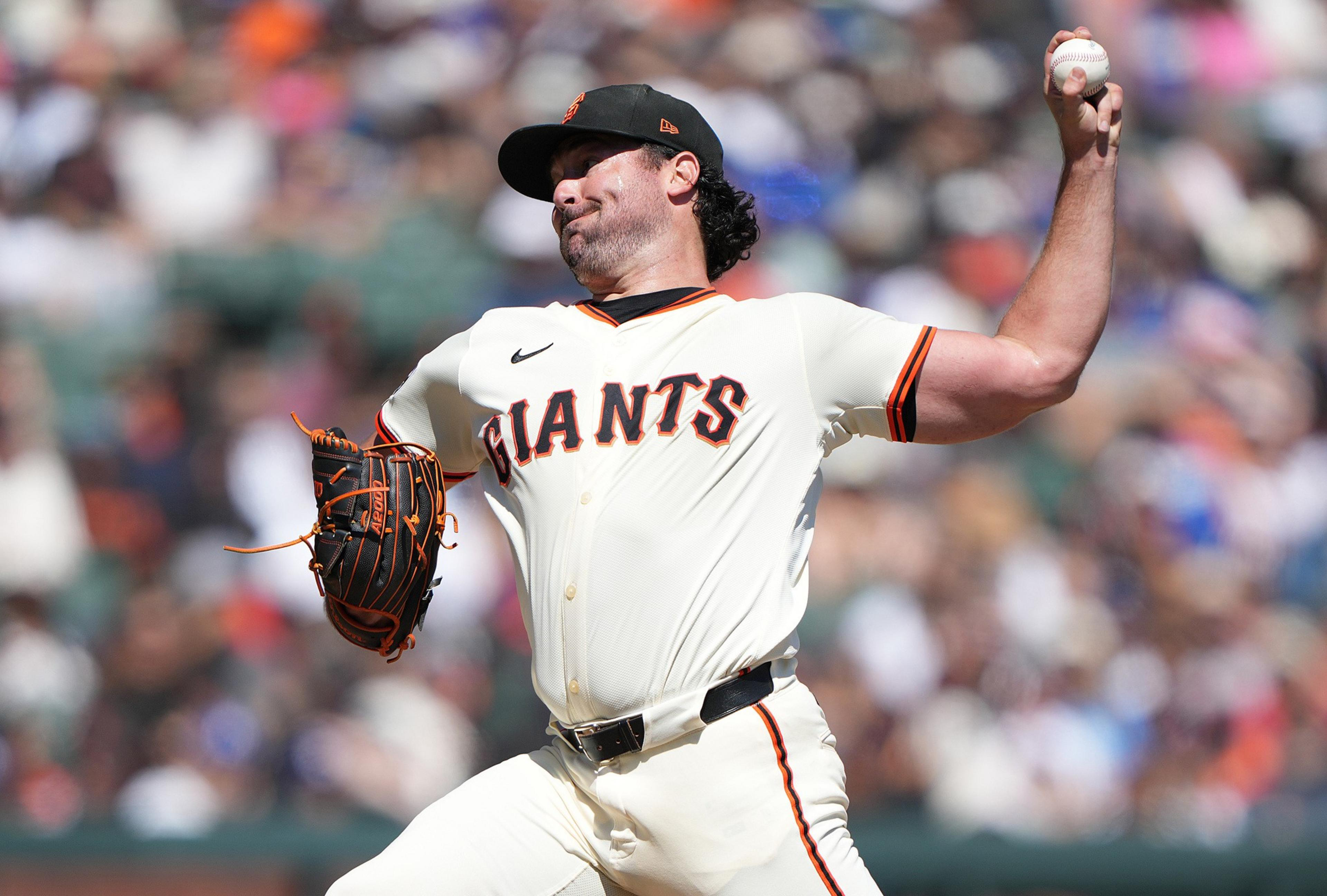 A baseball player wearing a Giants uniform pitches a ball, with his arm fully extended and his face showing focus during the throw.