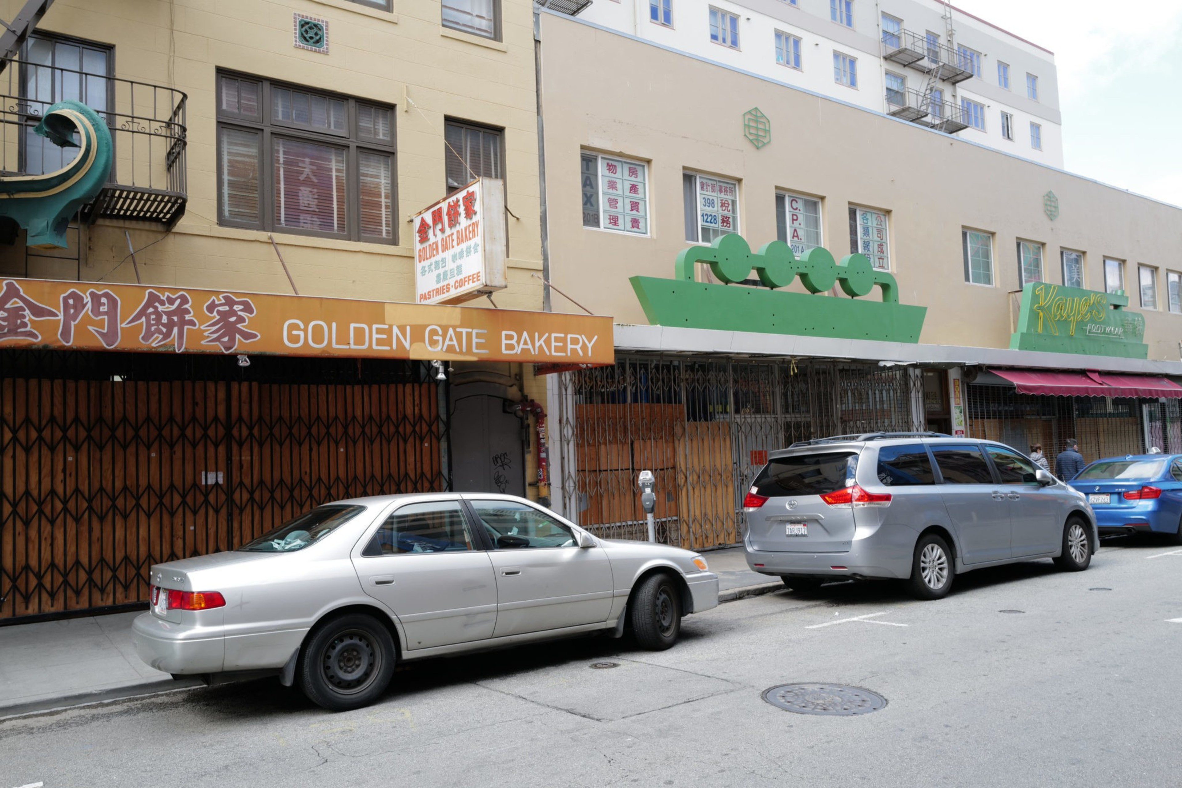 A street view with three parked cars in front of closed shops, including Golden Gate Bakery with a yellow-orange sign and Chinese characters.