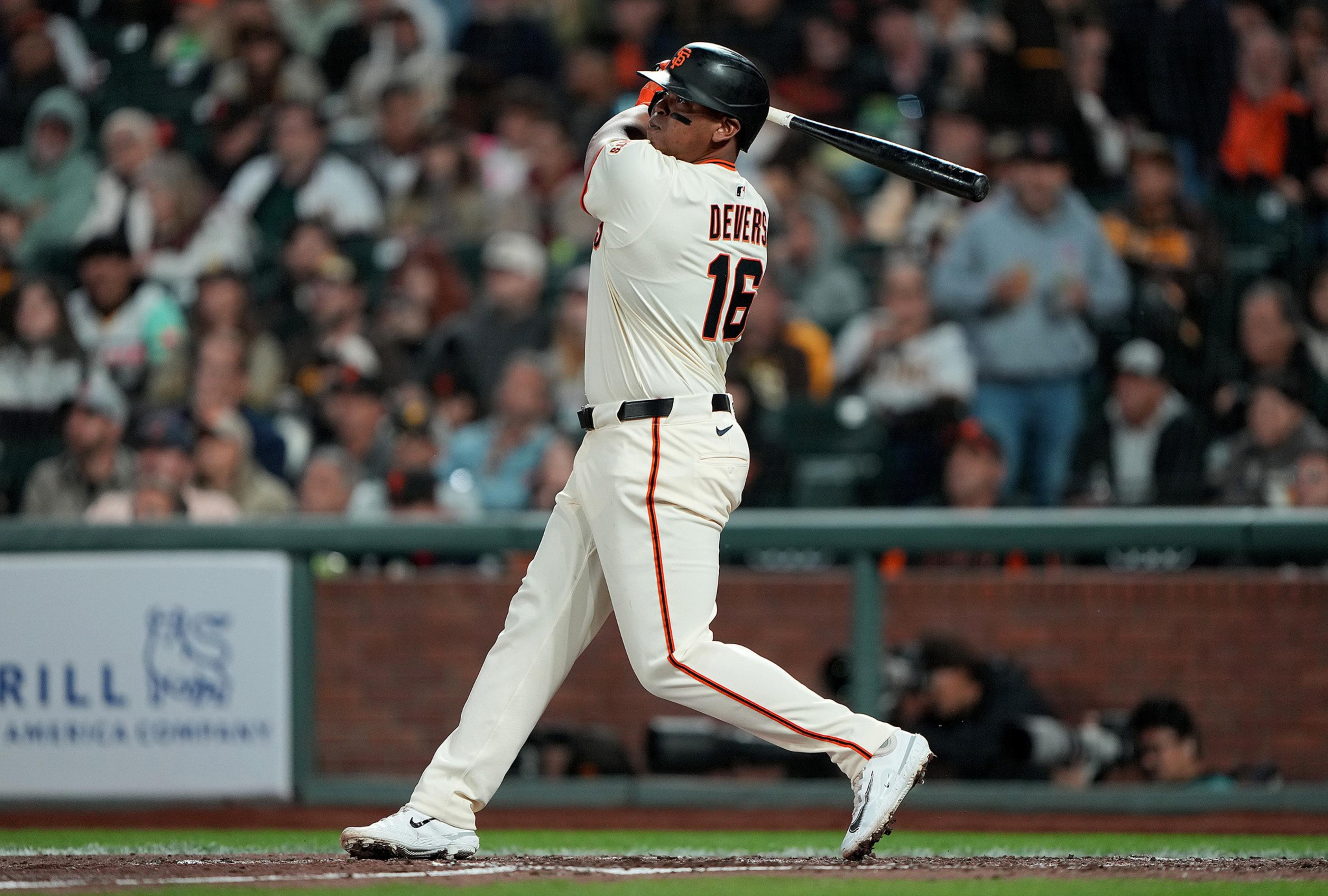 A baseball player wearing a white uniform with "Devers" and number 16 is swinging a bat during a game with spectators blurred in the background.