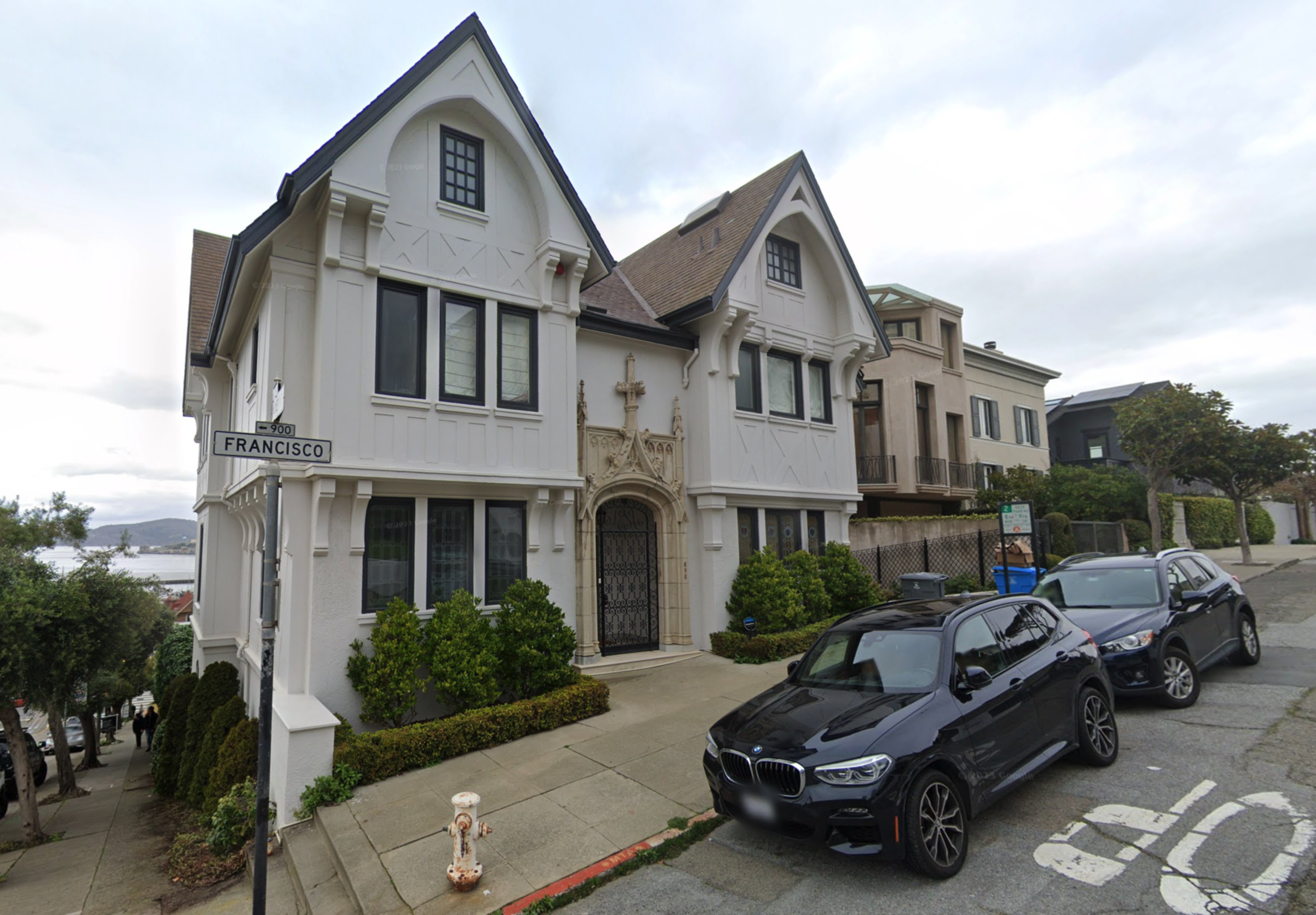 A three-story home painted white stands on a street corner.