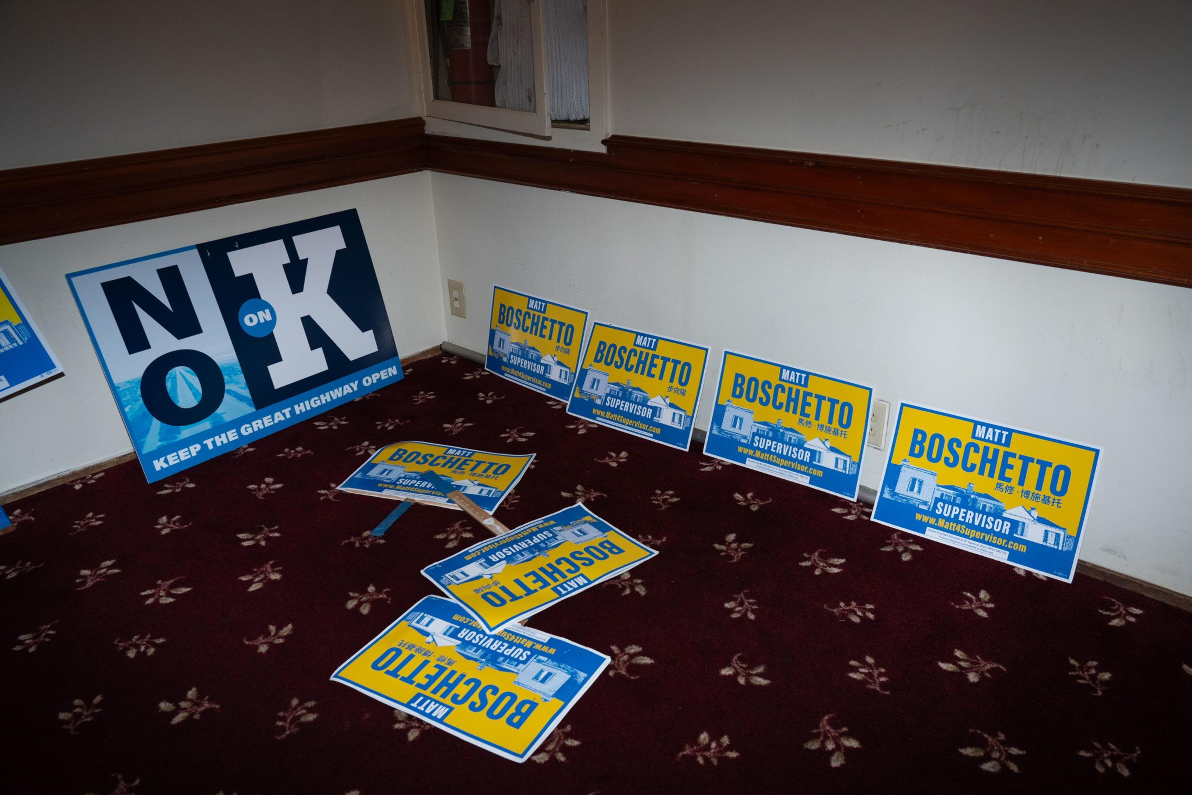 The image shows campaign signs on a carpeted floor. One large sign reads &quot;No on K&quot; and several smaller signs promote Matt Boschetto for Supervisor.