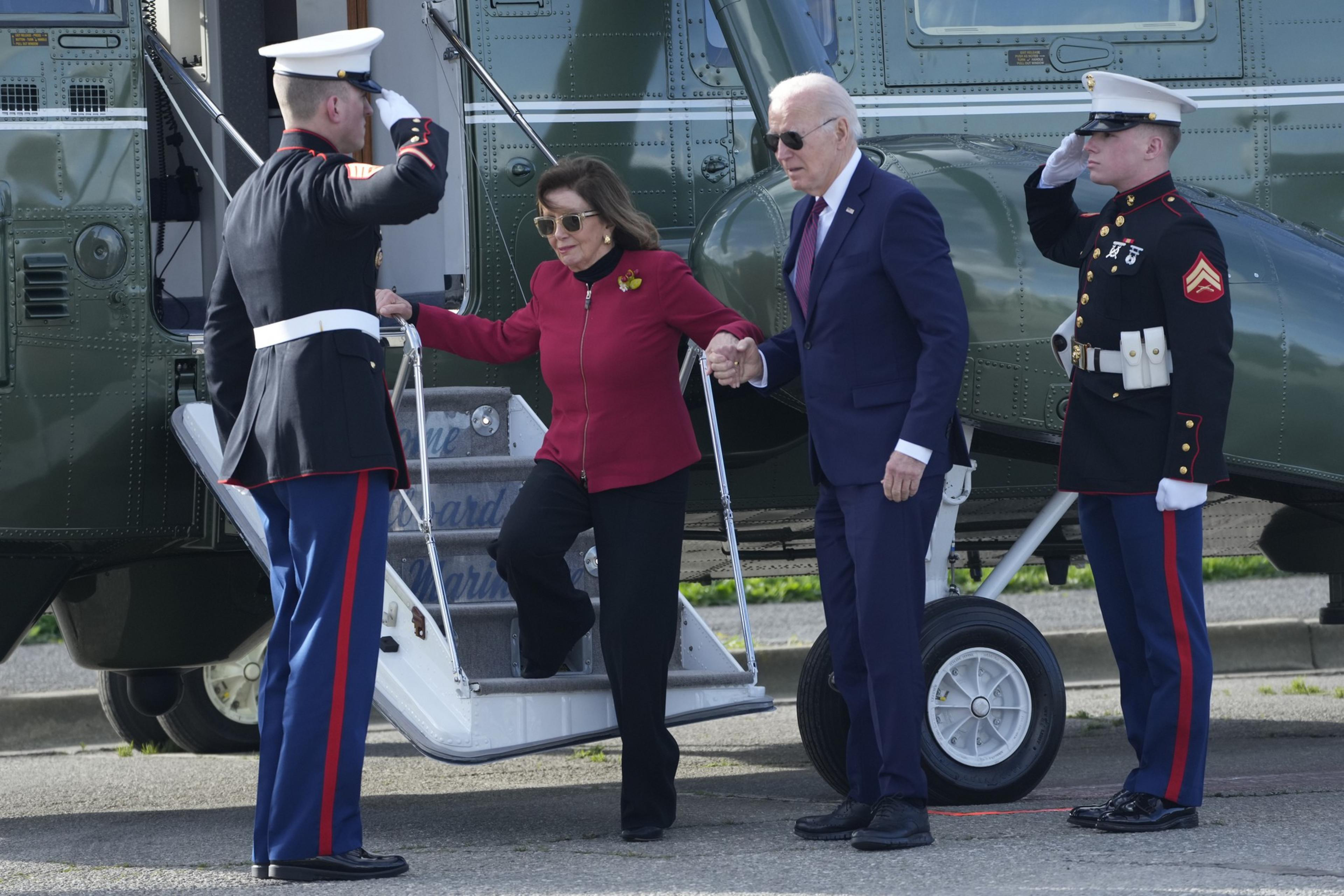 Nancy Pelosi steps off a helicopter with the help of President Joe Biden as two marines salute on either side.