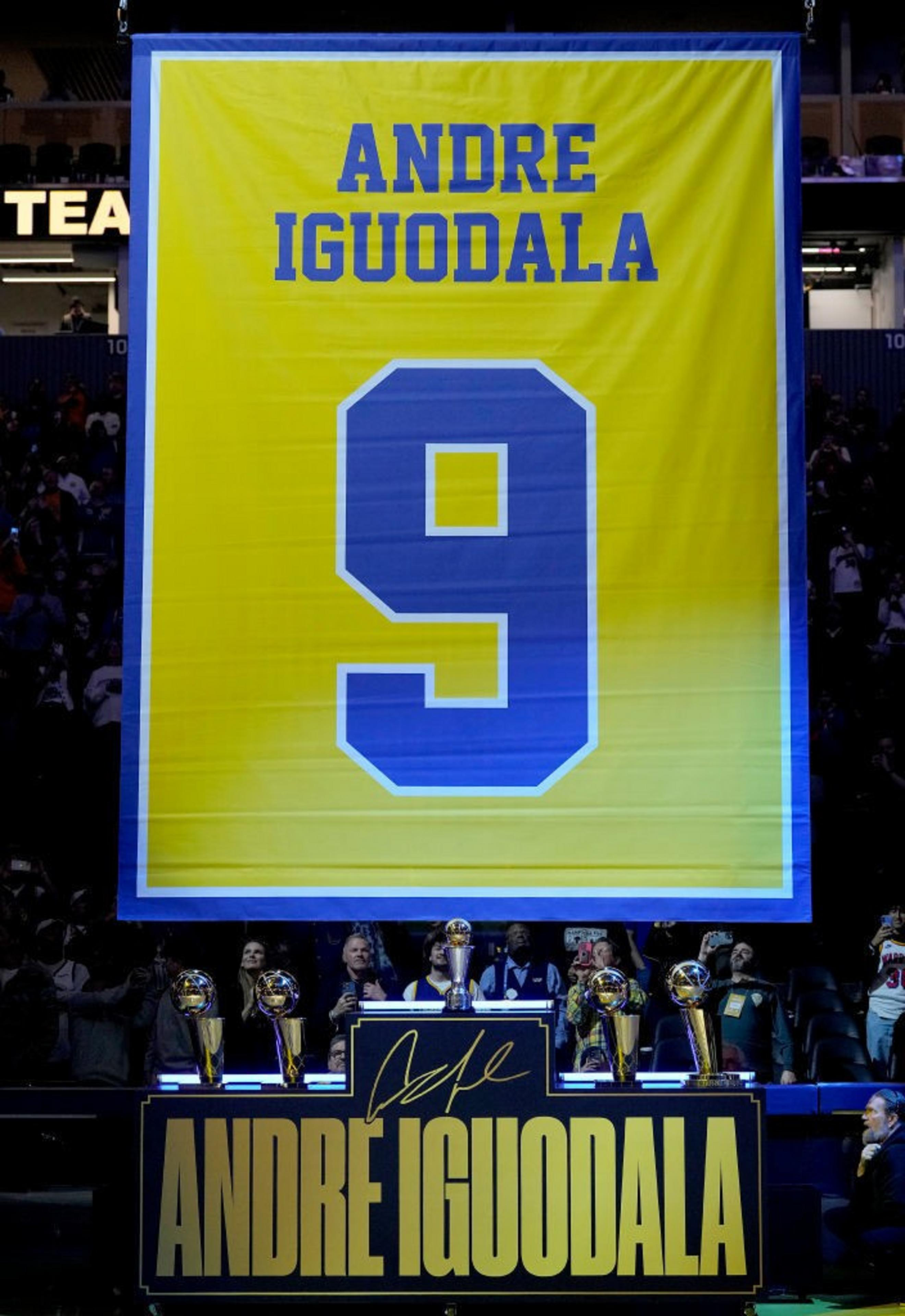 A large yellow banner with &quot;Andre Iguodala&quot; and the number &quot;9&quot; hangs prominently. Below, several trophies are displayed with a signed nameplate.