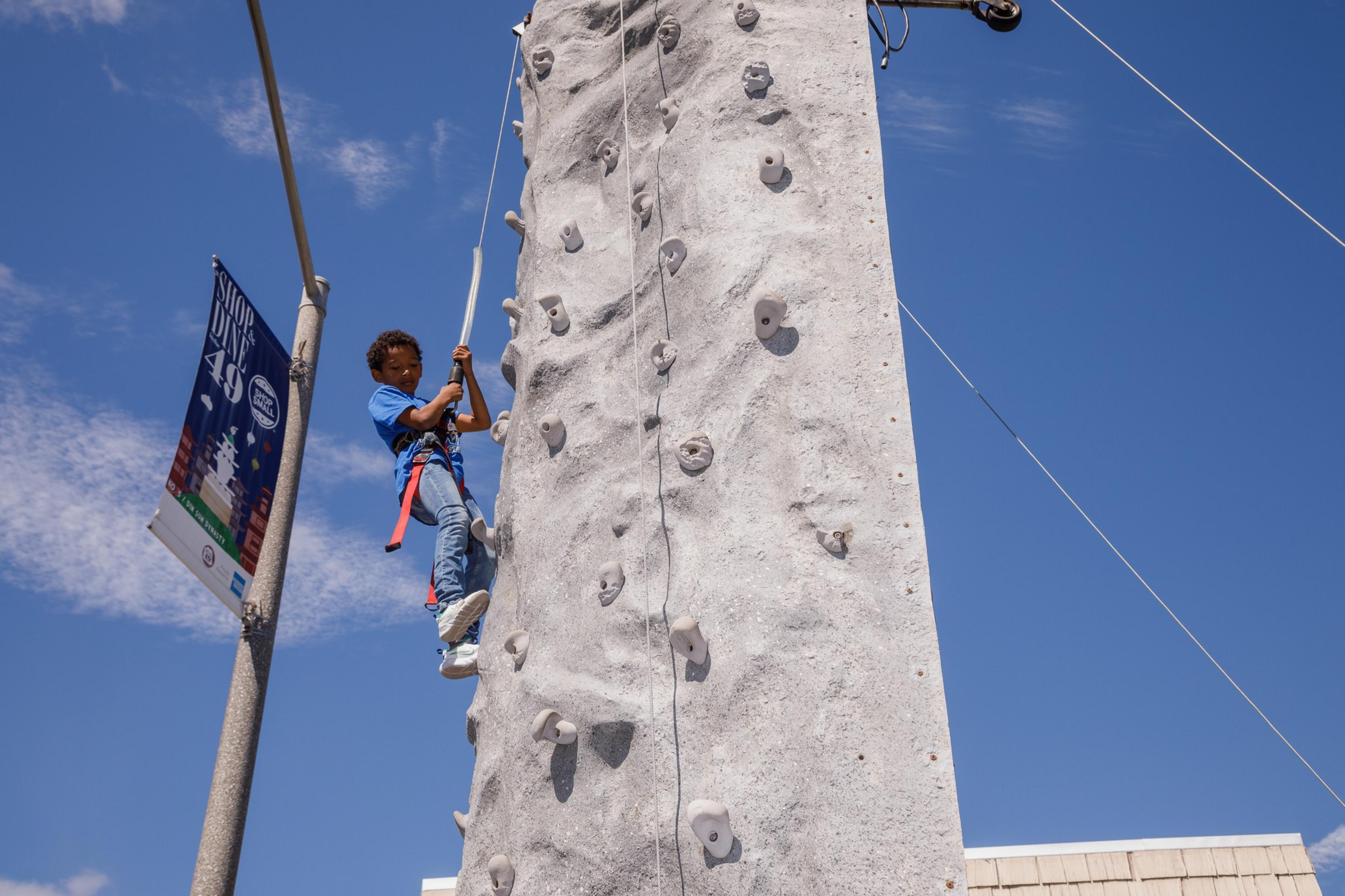 A child is climbing an outdoor artificial rock wall under a blue sky.