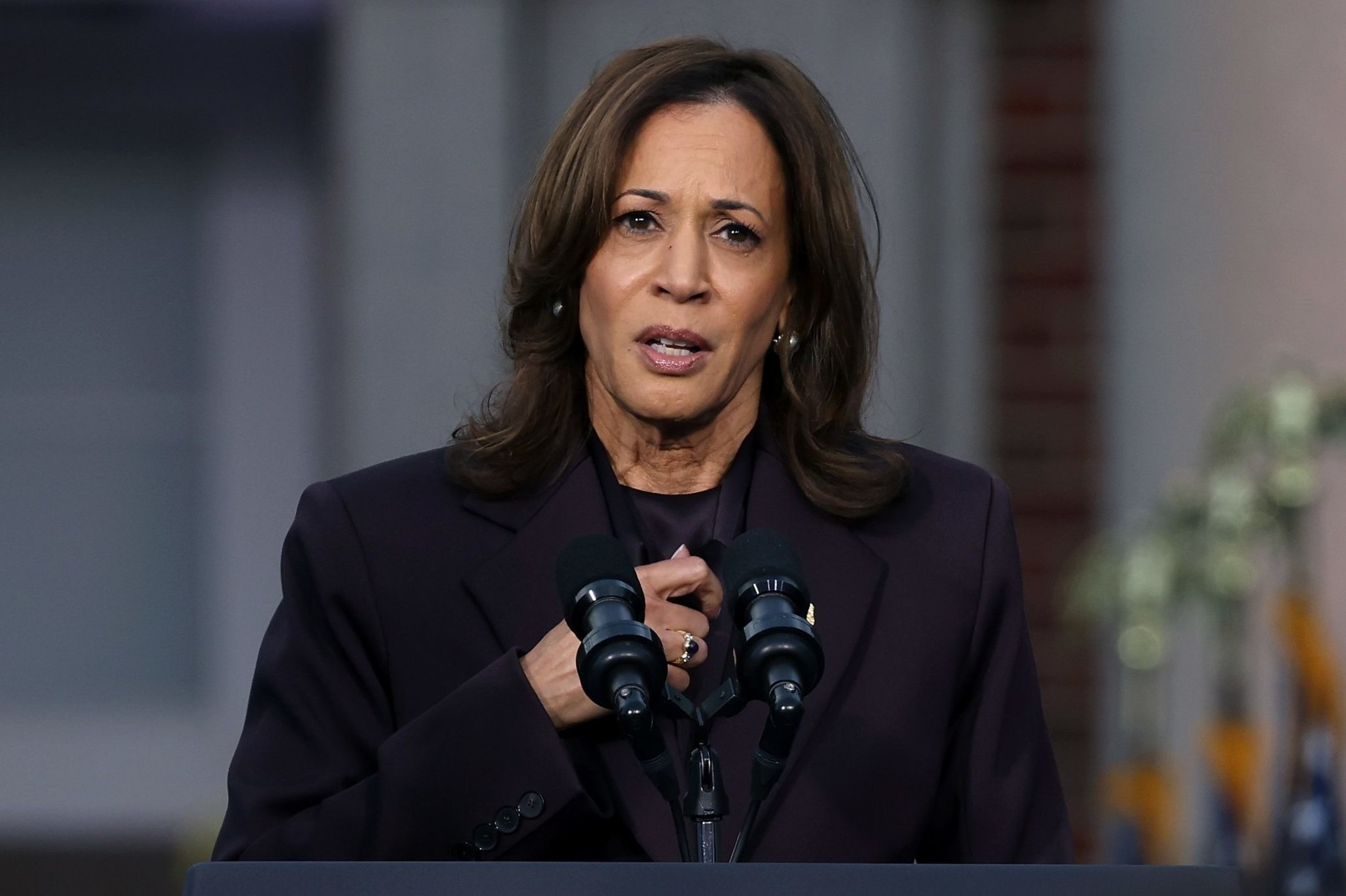 A woman in a dark suit speaks at a podium with &quot;Vice President of the United States&quot; seal. U.S. flags are blurred in the background, and she's speaking into microphones.