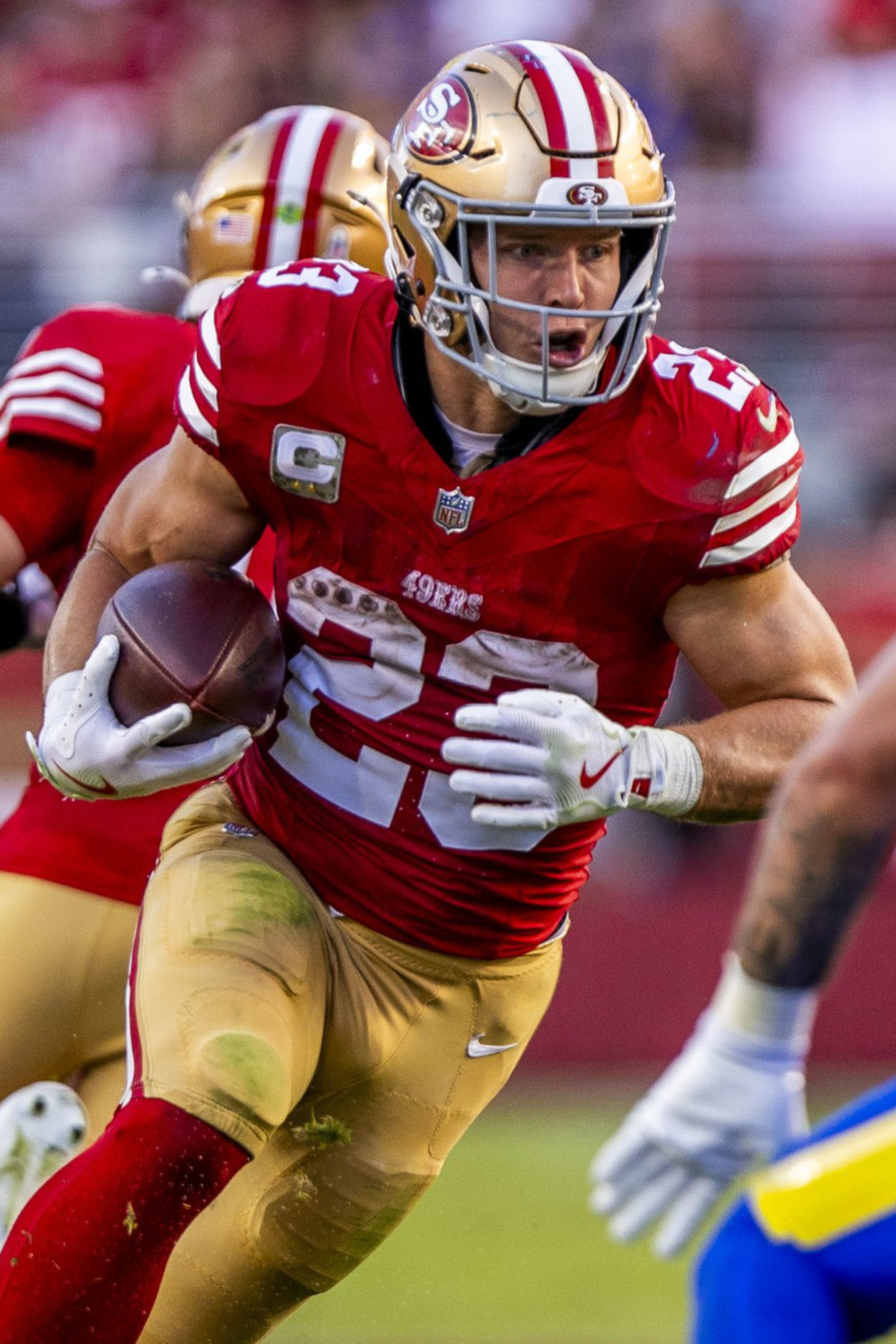 A San Francisco 49ers player runs with the ball while a Los Angeles Rams player prepares to tackle him during a football game.