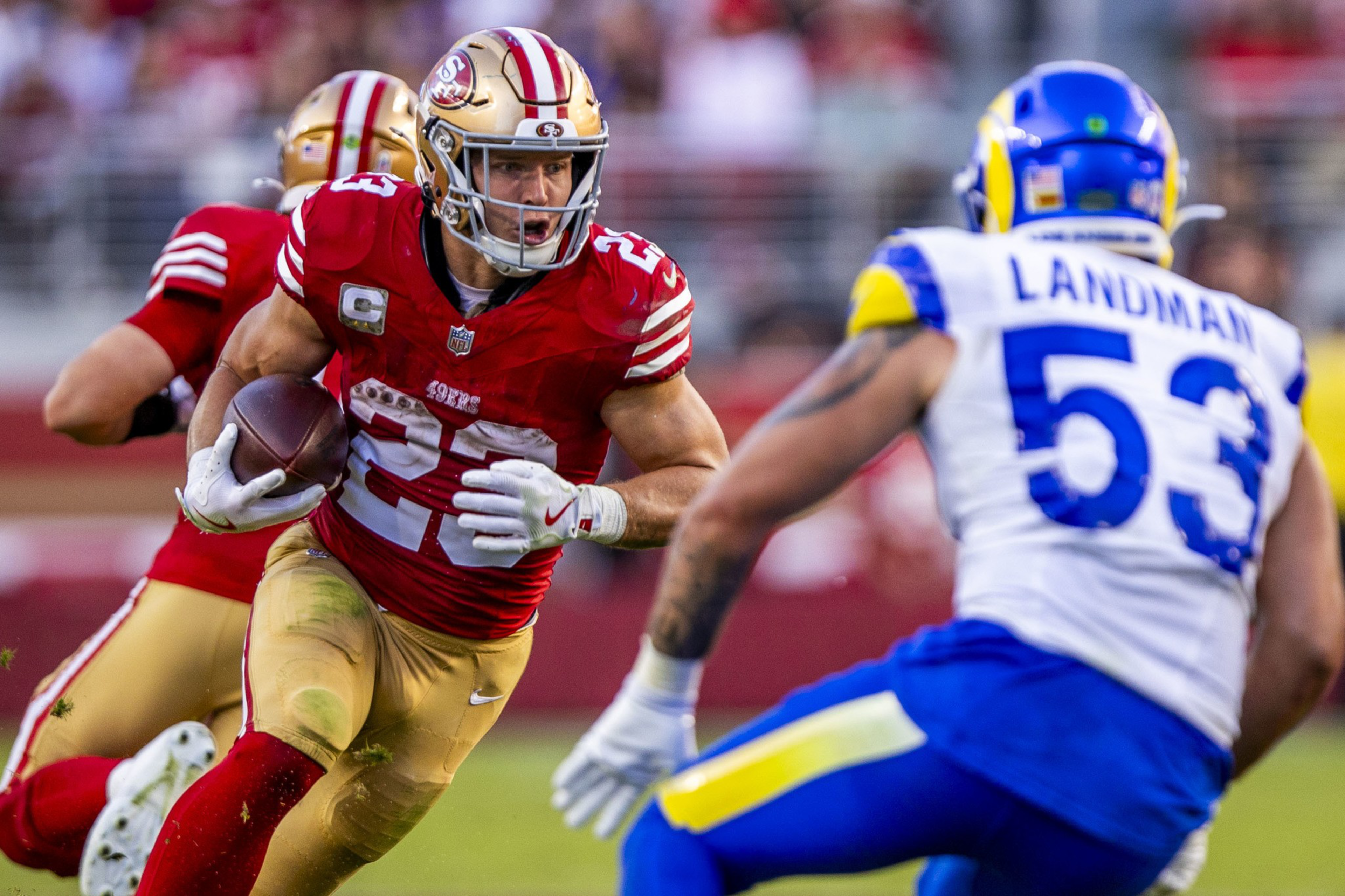 A San Francisco 49ers player runs with the ball while a Los Angeles Rams player prepares to tackle him during a football game.