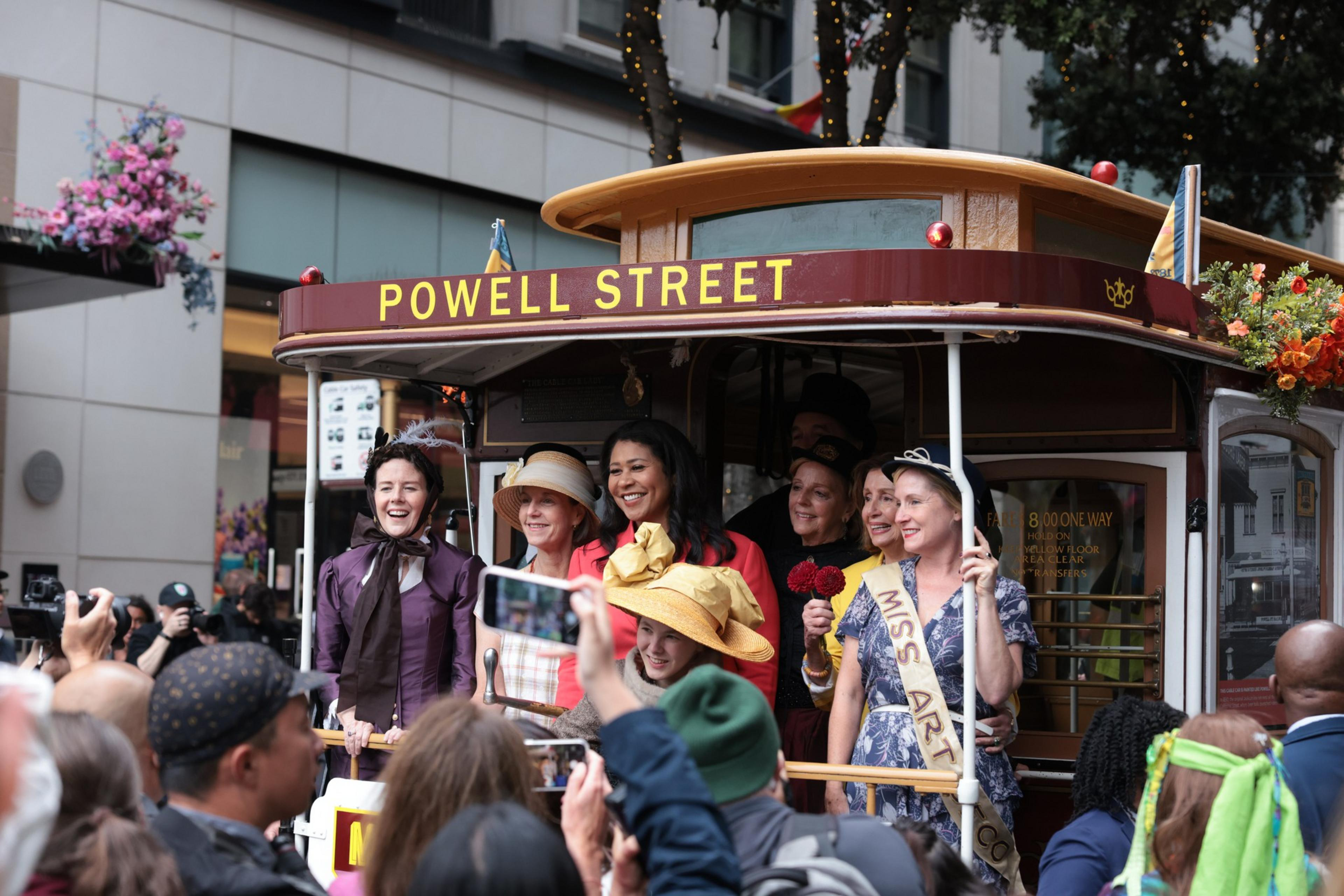 People stand on the back of a cable car and smile in San Francisco.