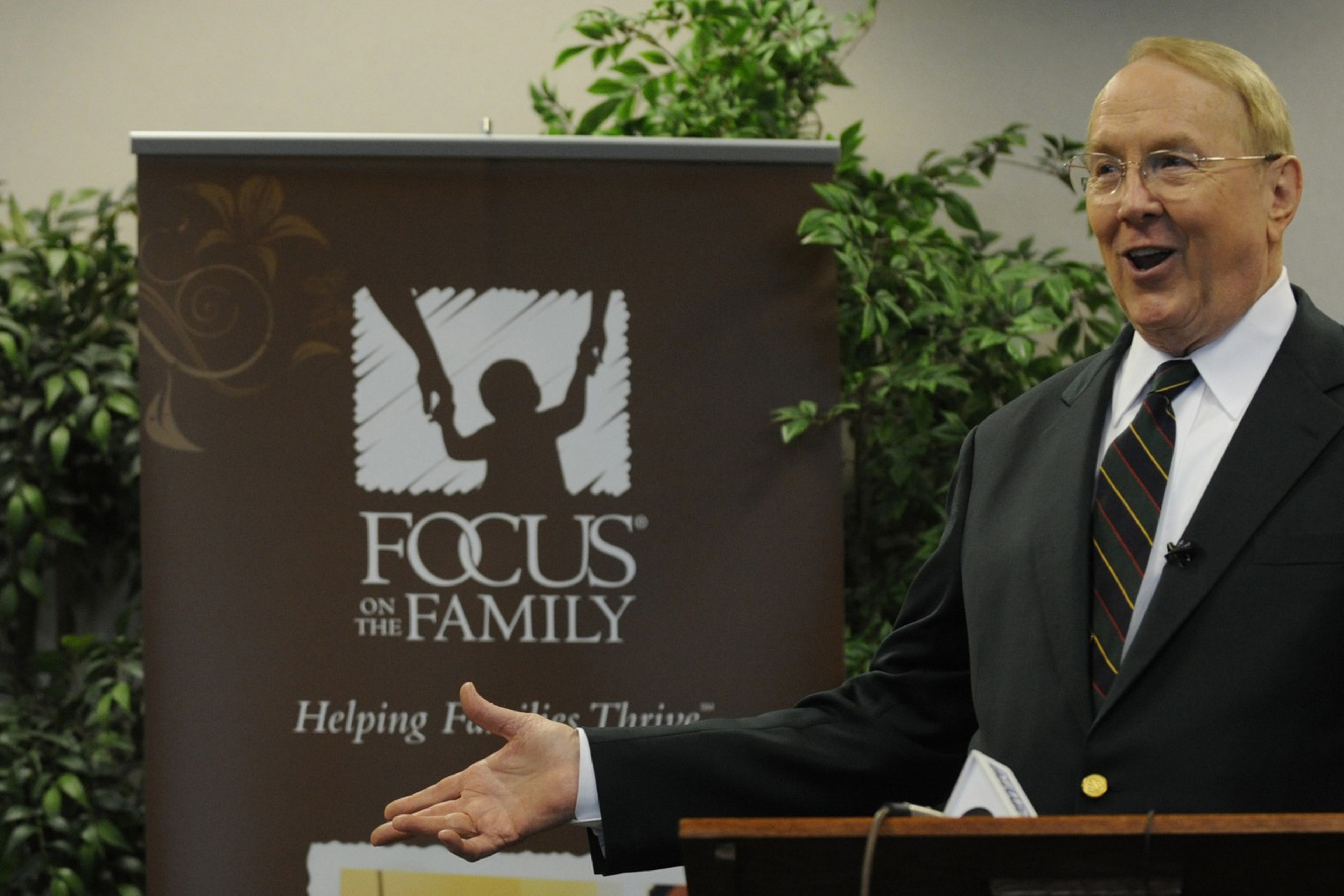 A man in a suit with a striped tie gestures while speaking at a podium, standing next to a banner that reads "Focus on the Family."