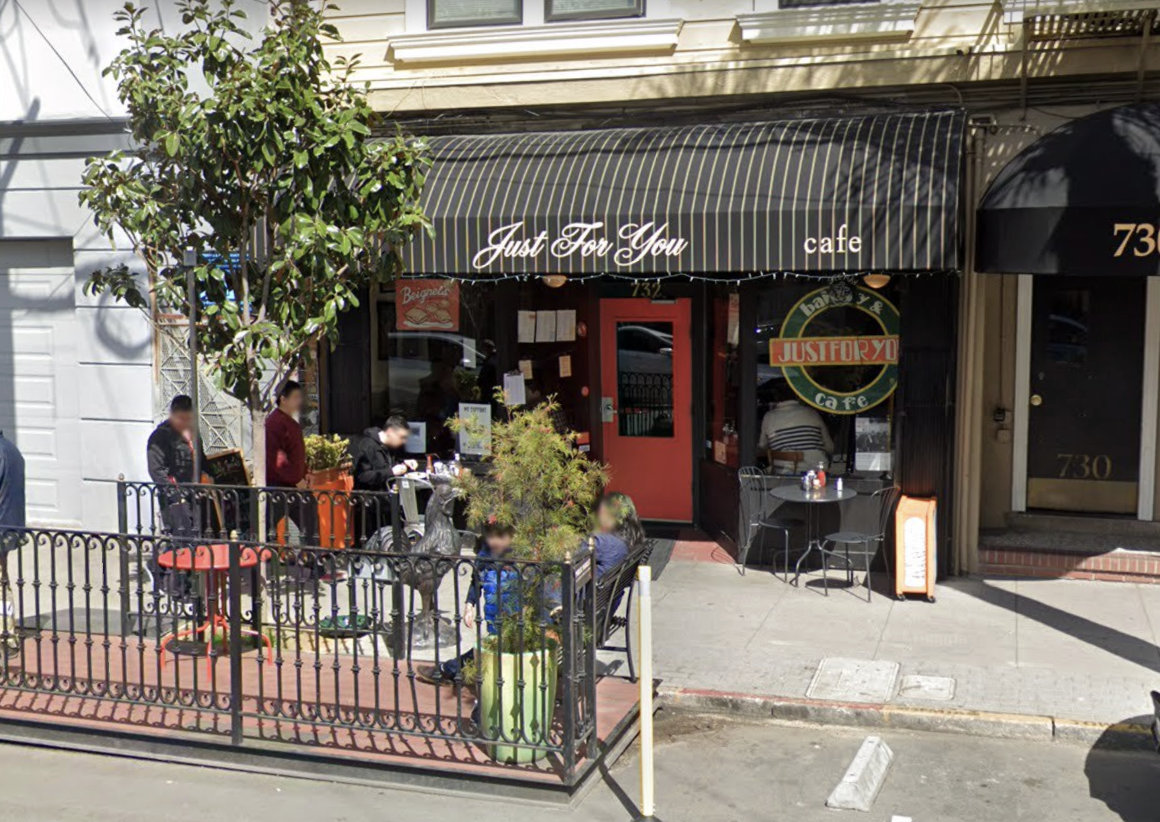 A cafe named "Just For You" with a black and white striped awning, red door, outdoor seating, and several people sitting and standing nearby.