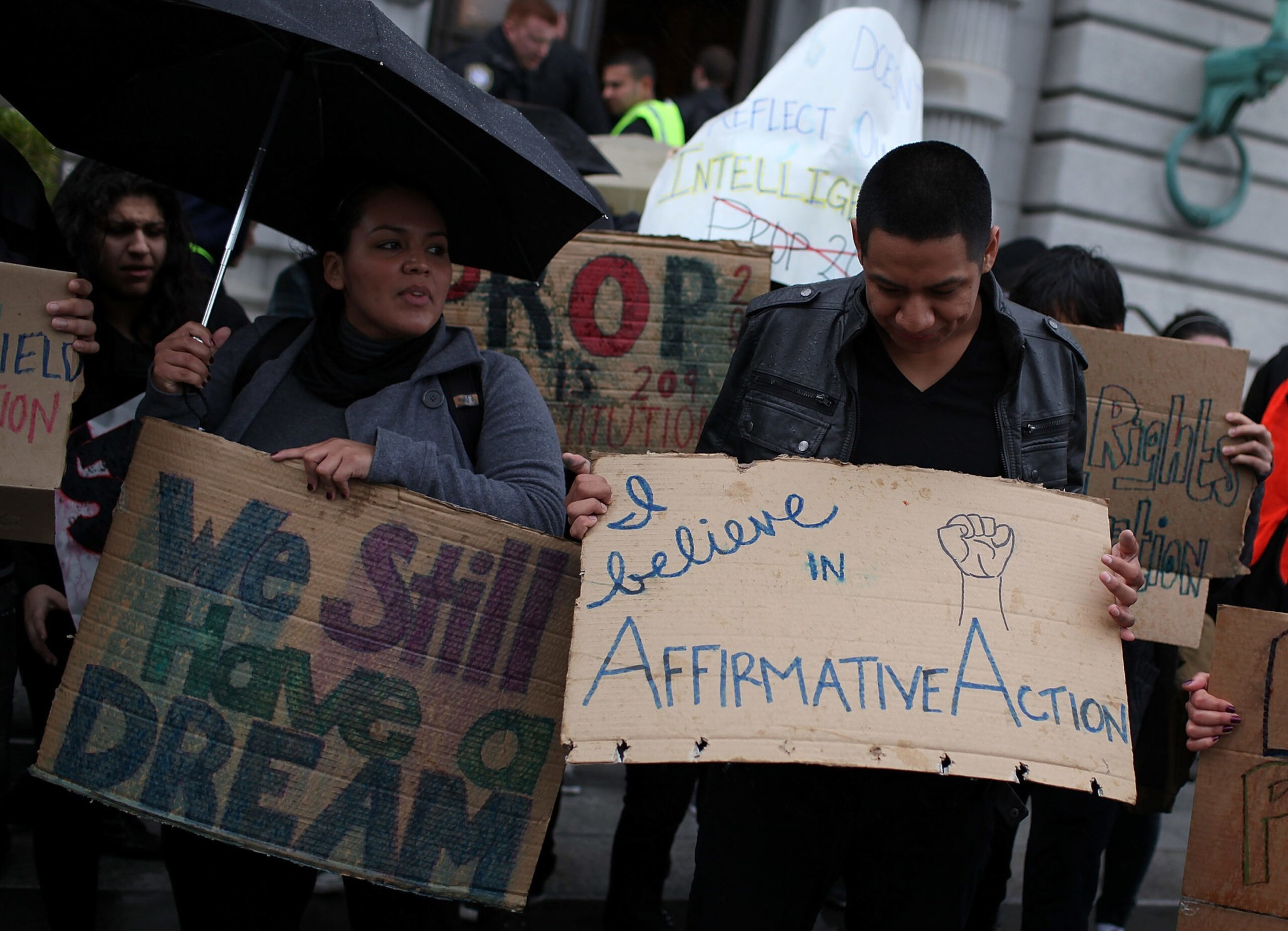 People hold handmade cardboard signs reading "We Still Have a Dream" and "I believe in Affirmative Action" during a protest.