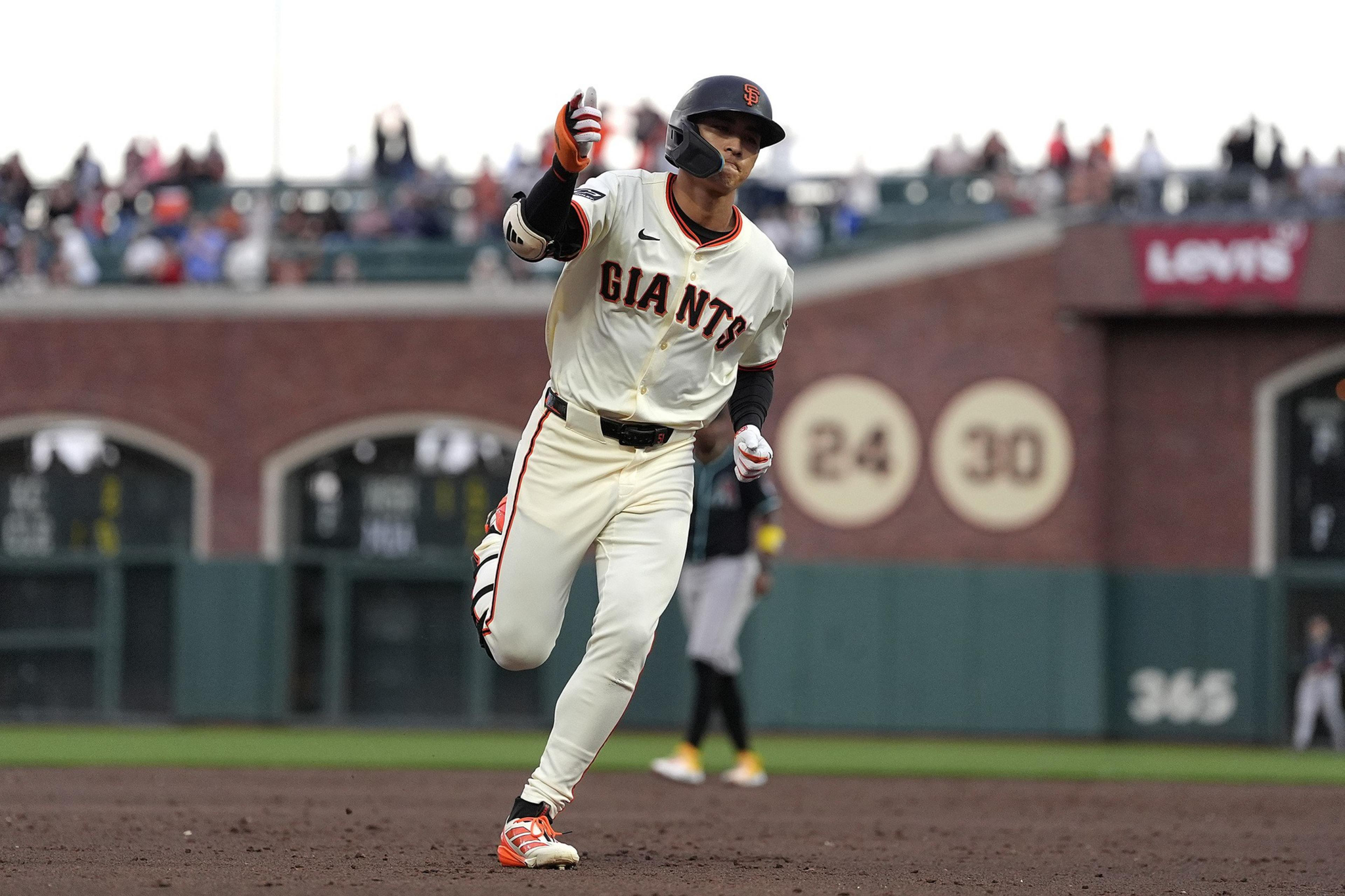 A Giants baseball player is running on the field, raising his right hand in celebration, wearing a helmet and uniform with the number partially visible.