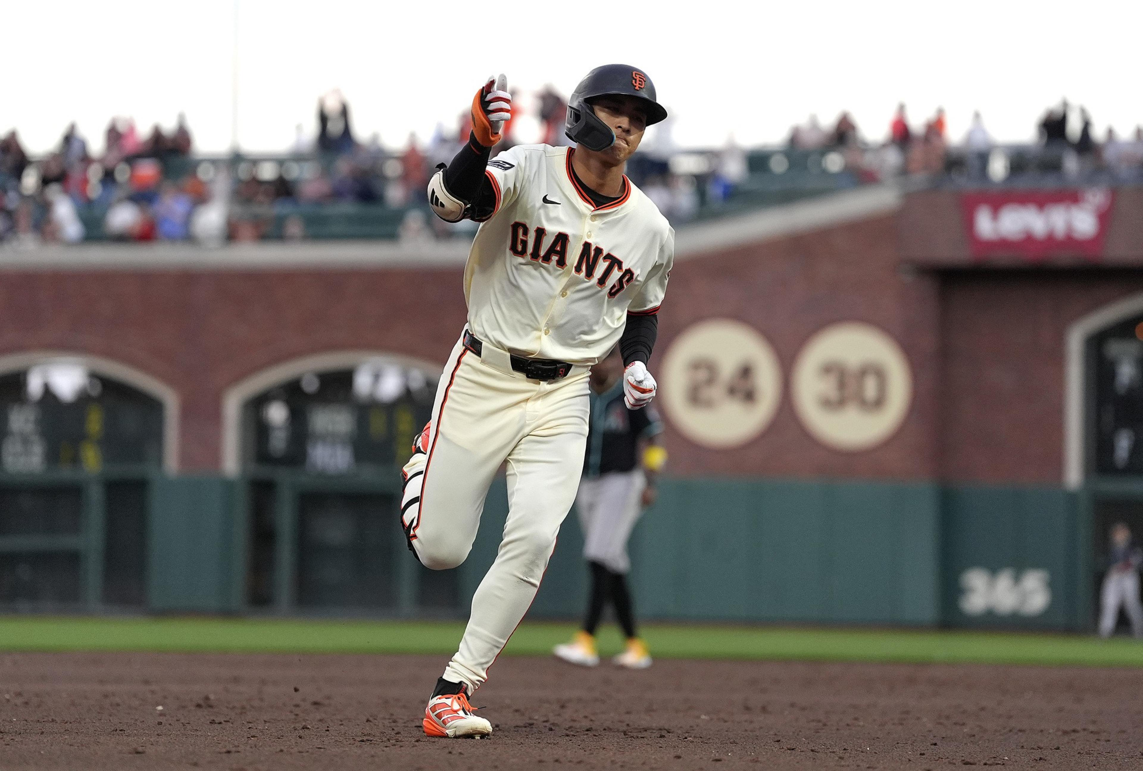 A Giants baseball player is running on the field, raising his right hand in celebration, wearing a helmet and uniform with the number partially visible.