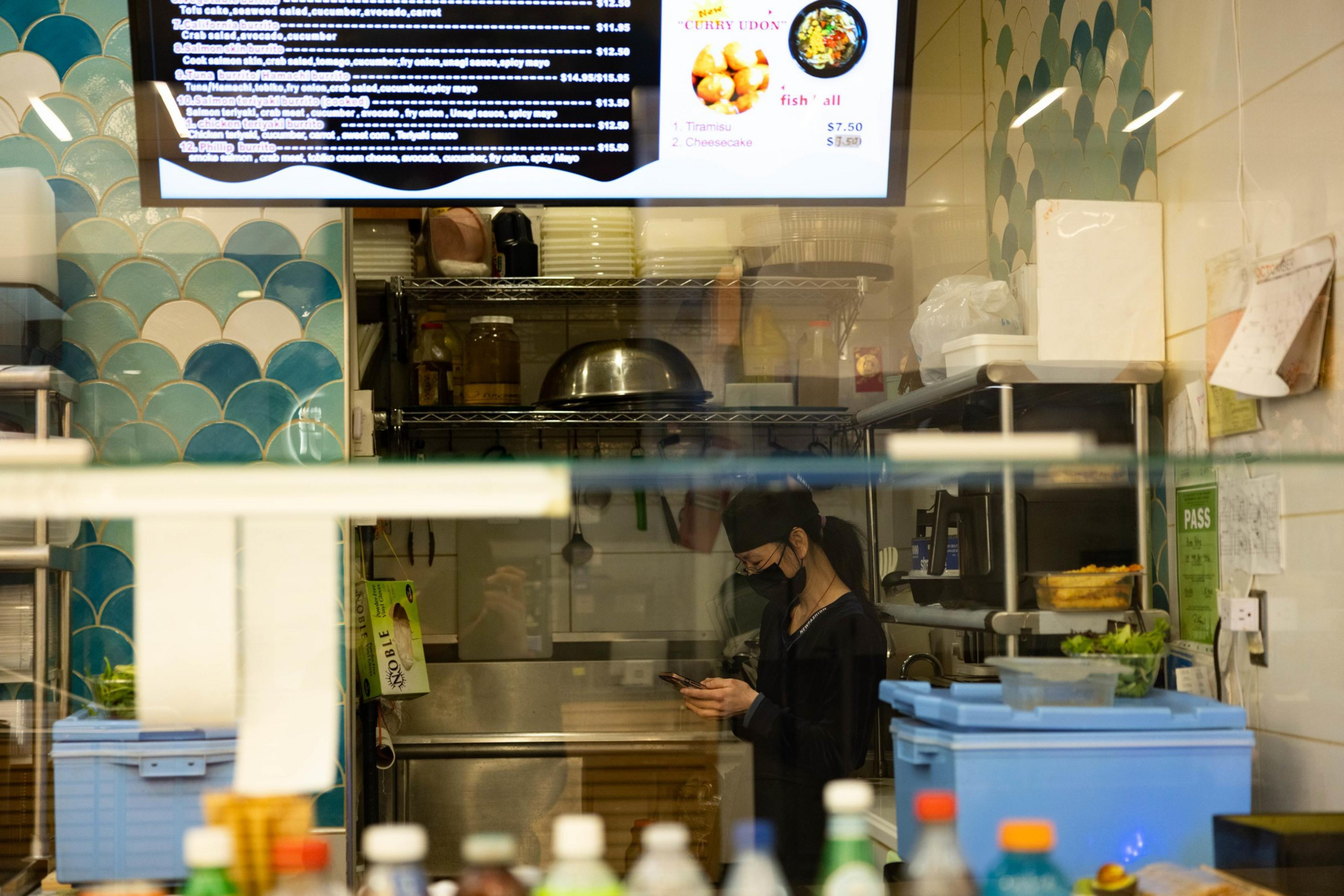 A restaurant worker behind an empty counter texts on her phone. 