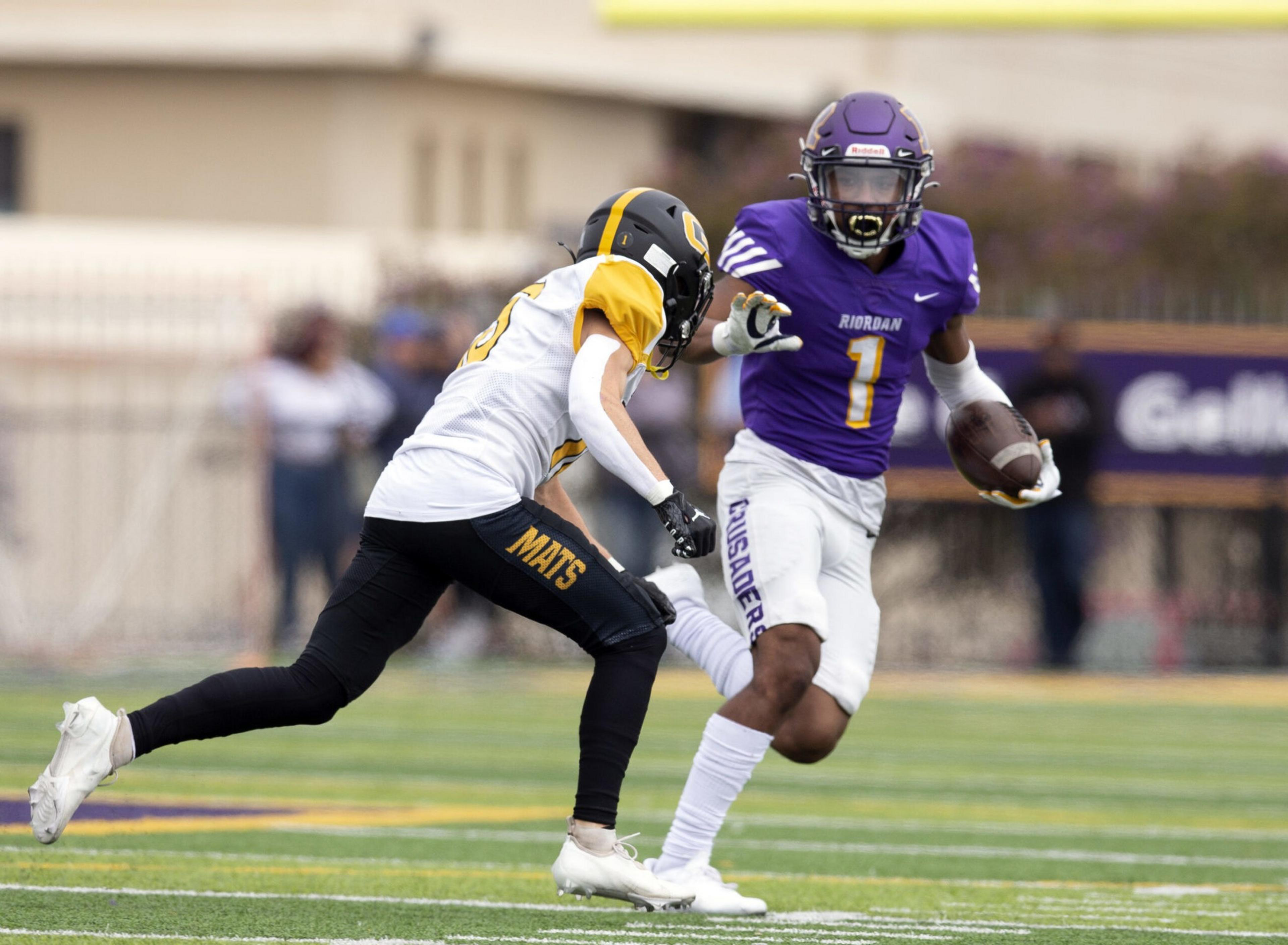 A football player in a purple uniform runs with the ball while a player in a white and yellow uniform attempts to tackle him on the field.