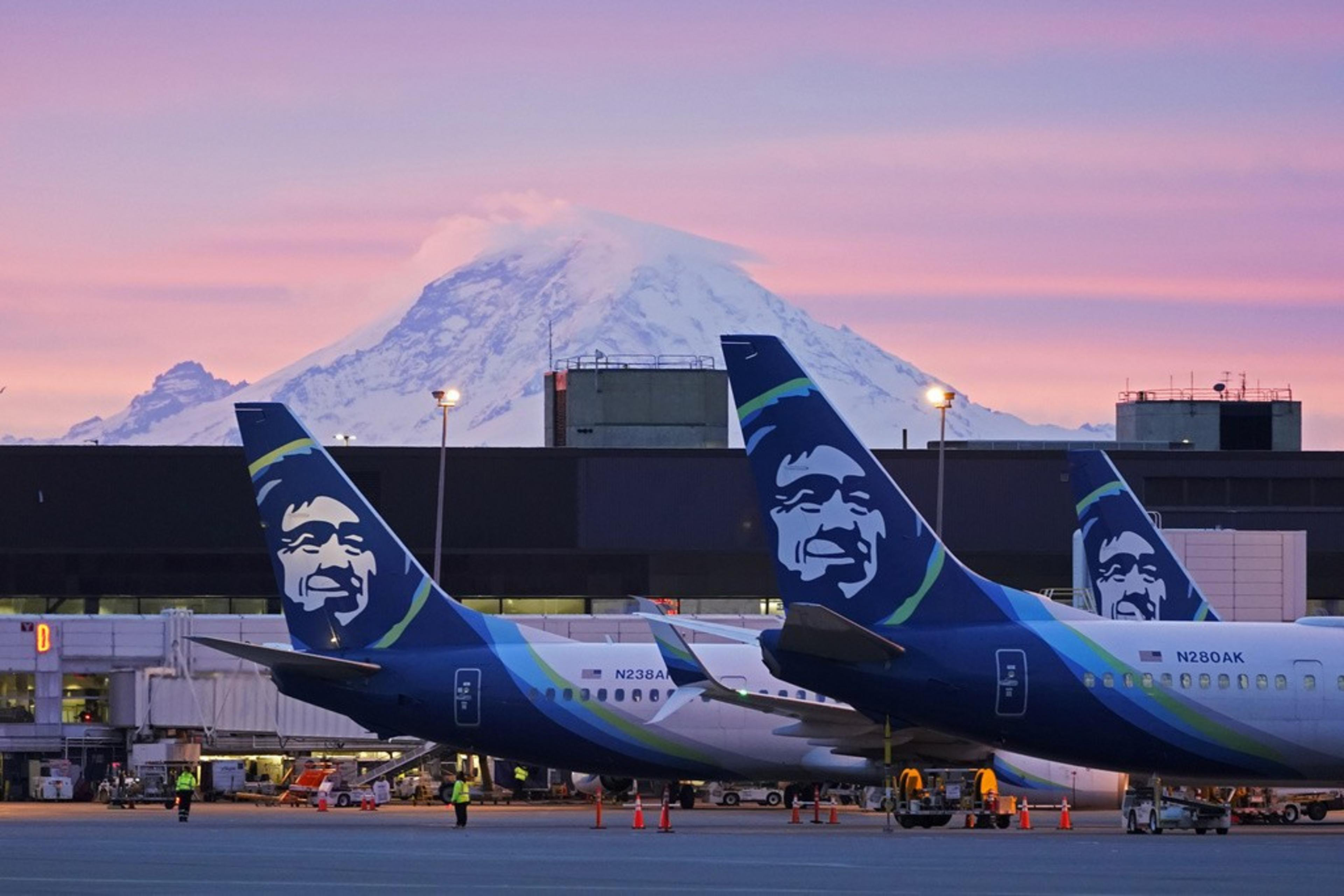 Two airplanes parked on a runway with mountains in the background.