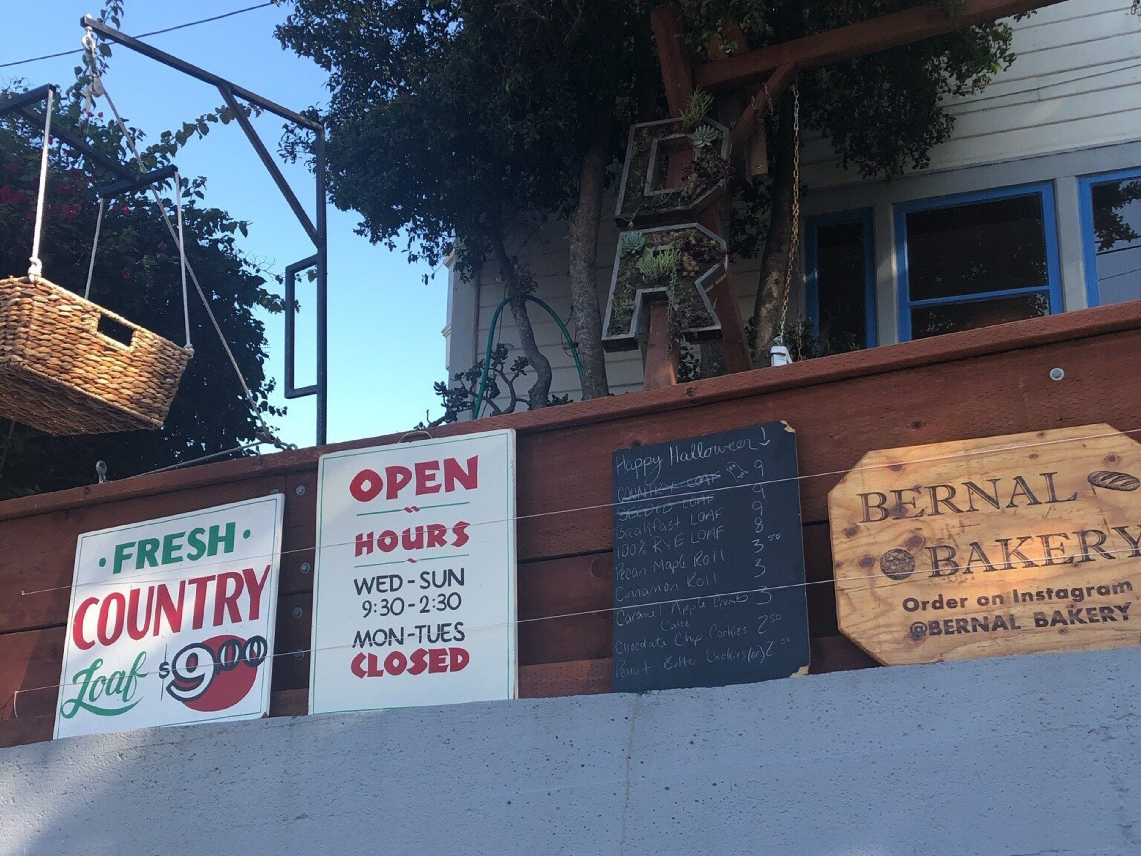 A wicker basket dangles next to signs for a bakery.