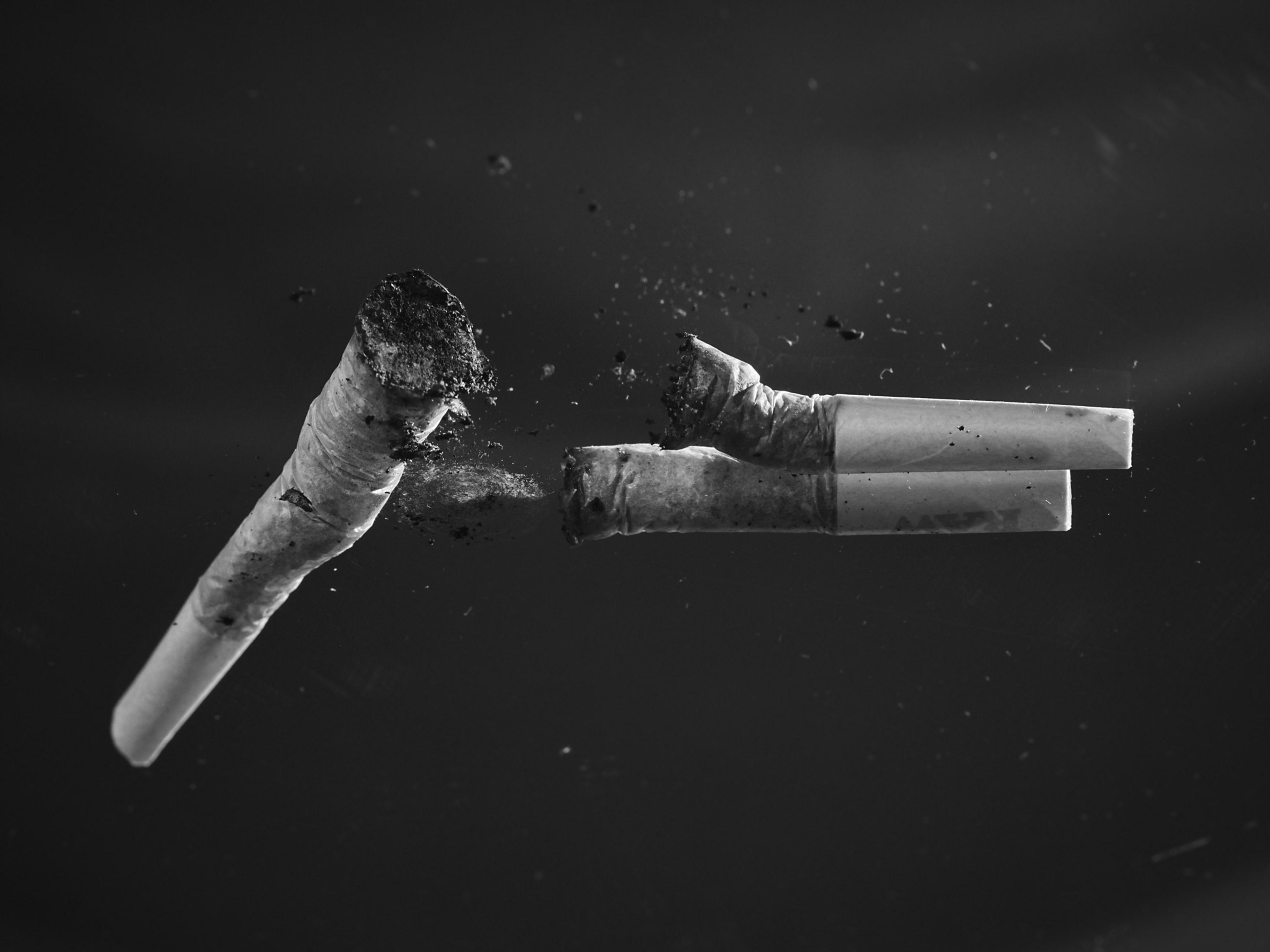 Two joints break apart in mid-air against a dark background, with ash and weed scattering between them.