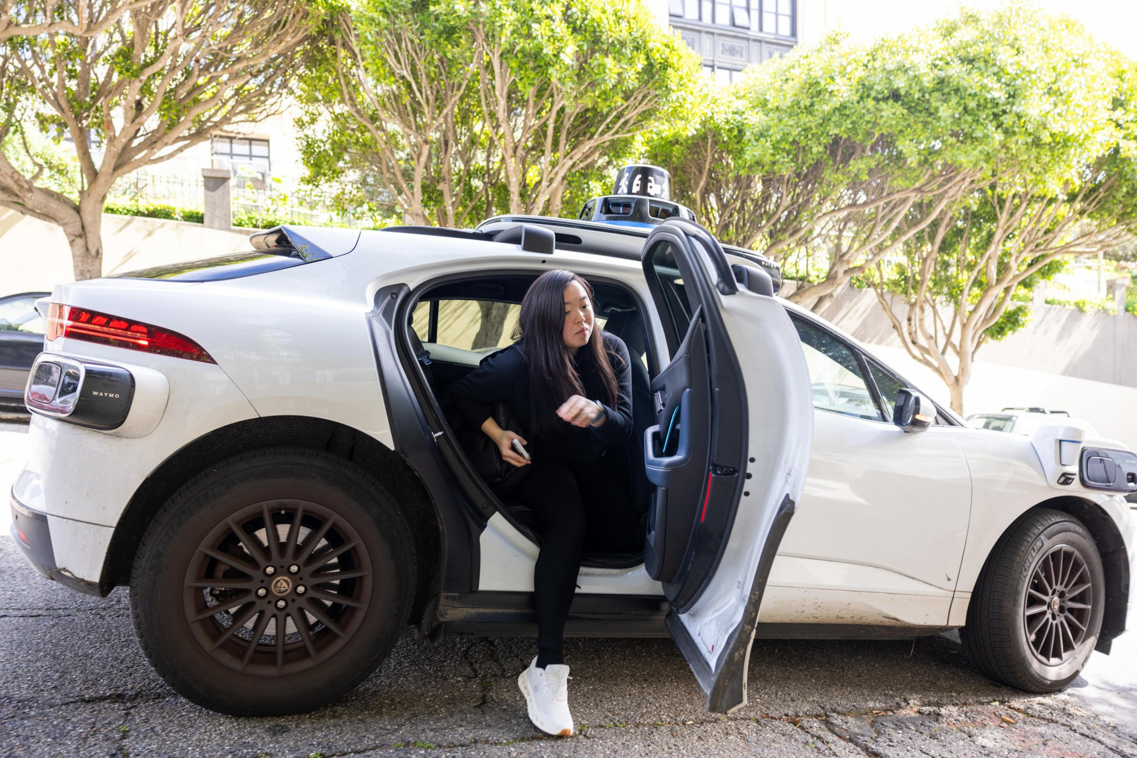 A self-driving vehicle's rooftop sensor array is shown in front of a modern multi-story apartment building with glass balconies.