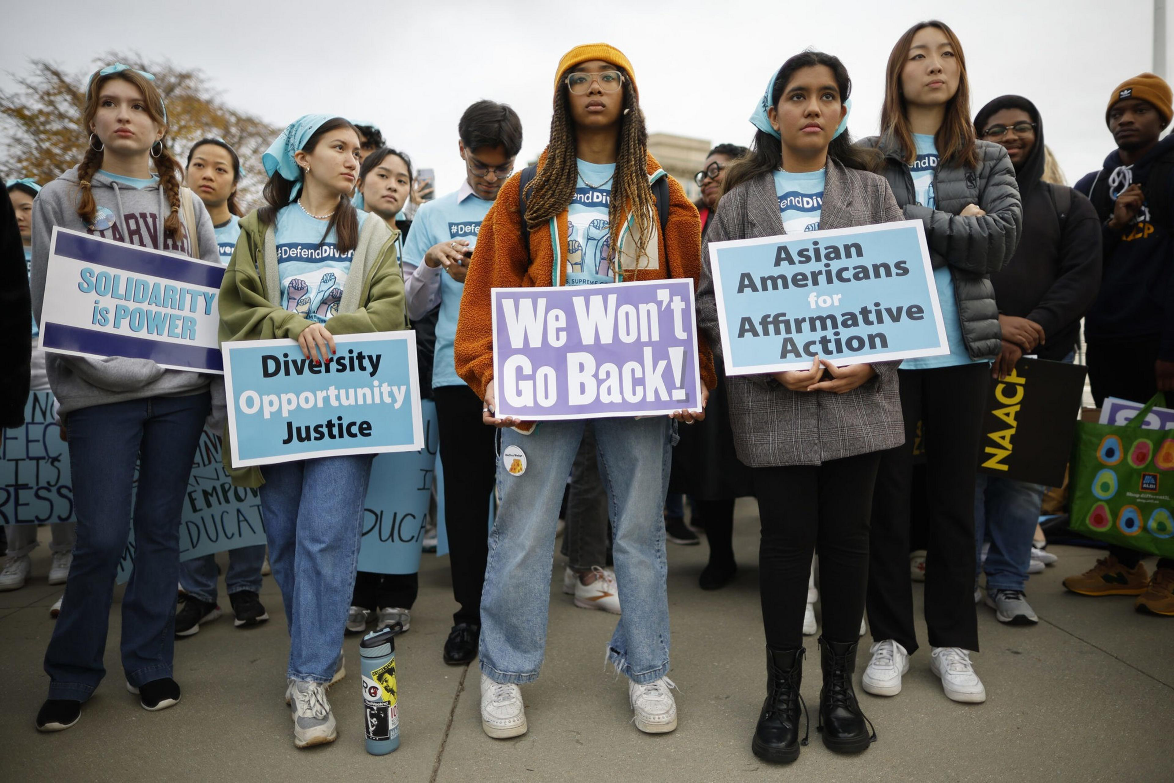A group of diverse young people stand holding signs advocating for solidarity, diversity, affirmative action, and refusing to go backward.