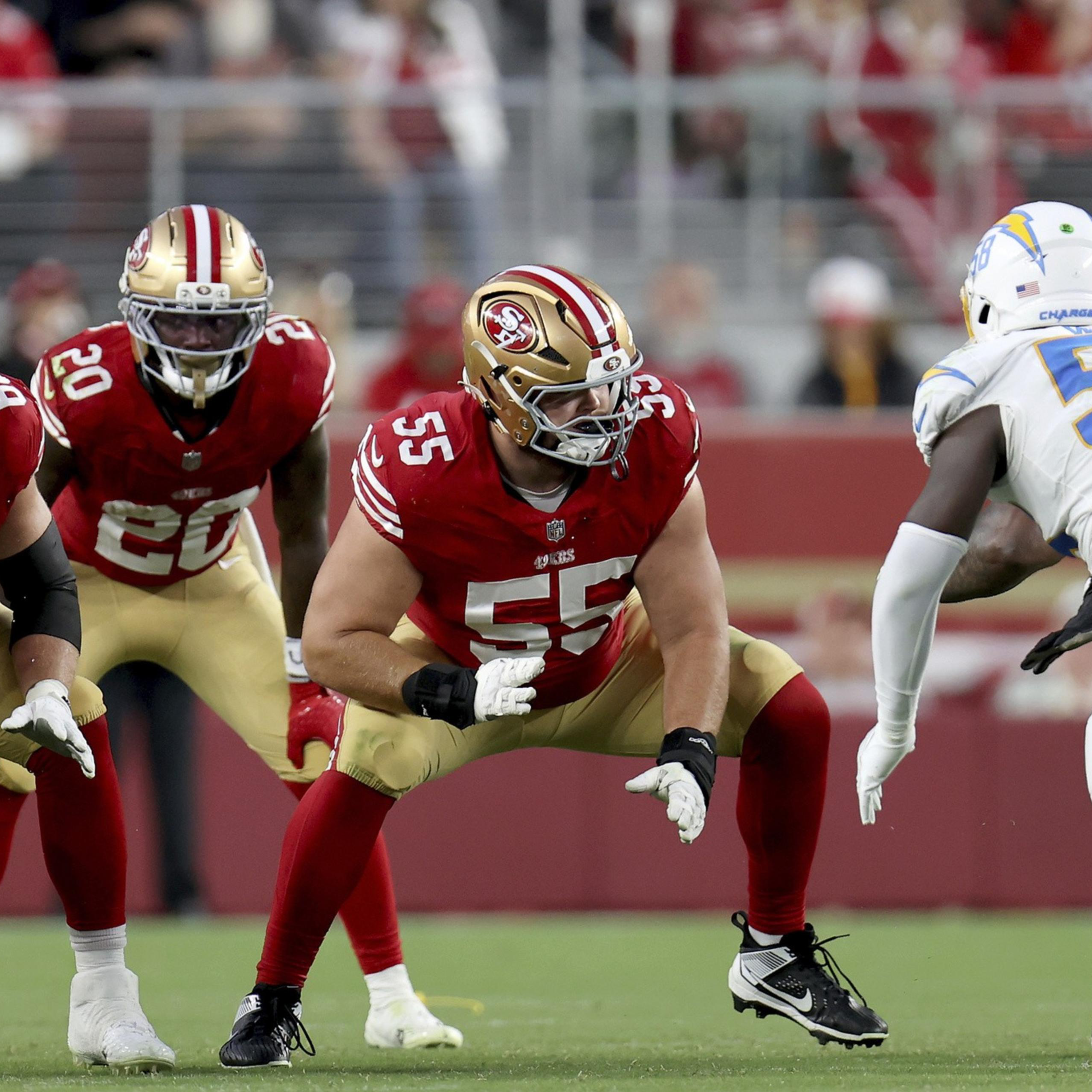 Football players from the San Francisco 49ers in red and gold jerseys face off against Los Angeles Chargers players in white and blue uniforms on the field.